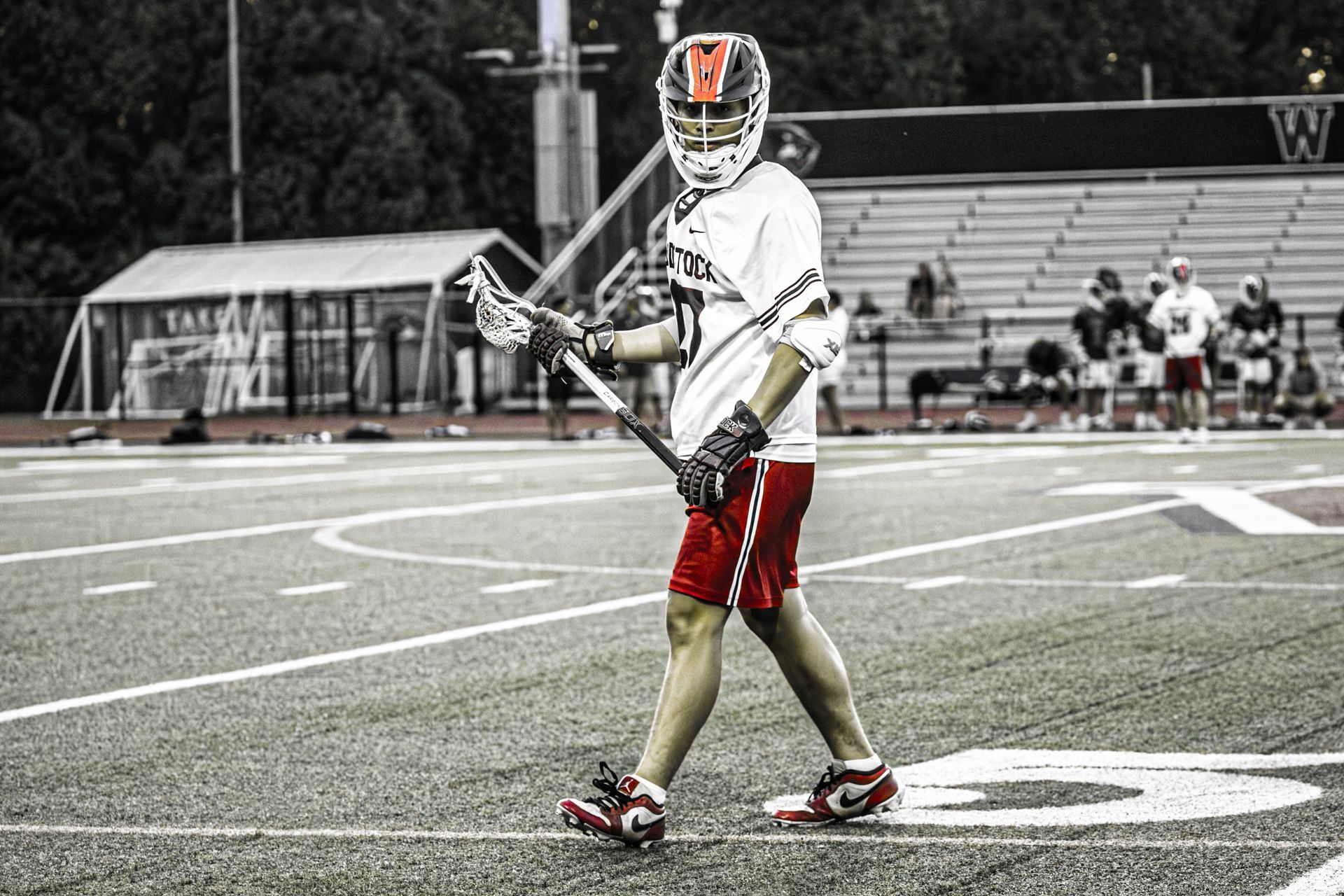 Lacrosse player in white and red uniform walking on a field during a game.