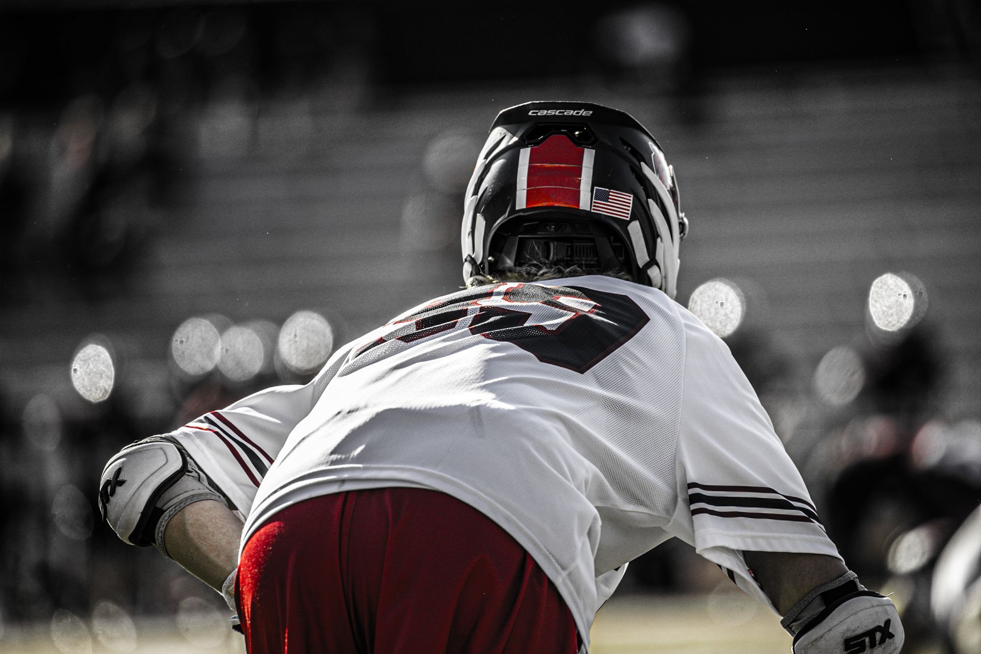 Football player in white jersey crouches on field under stadium lights, seen from behind