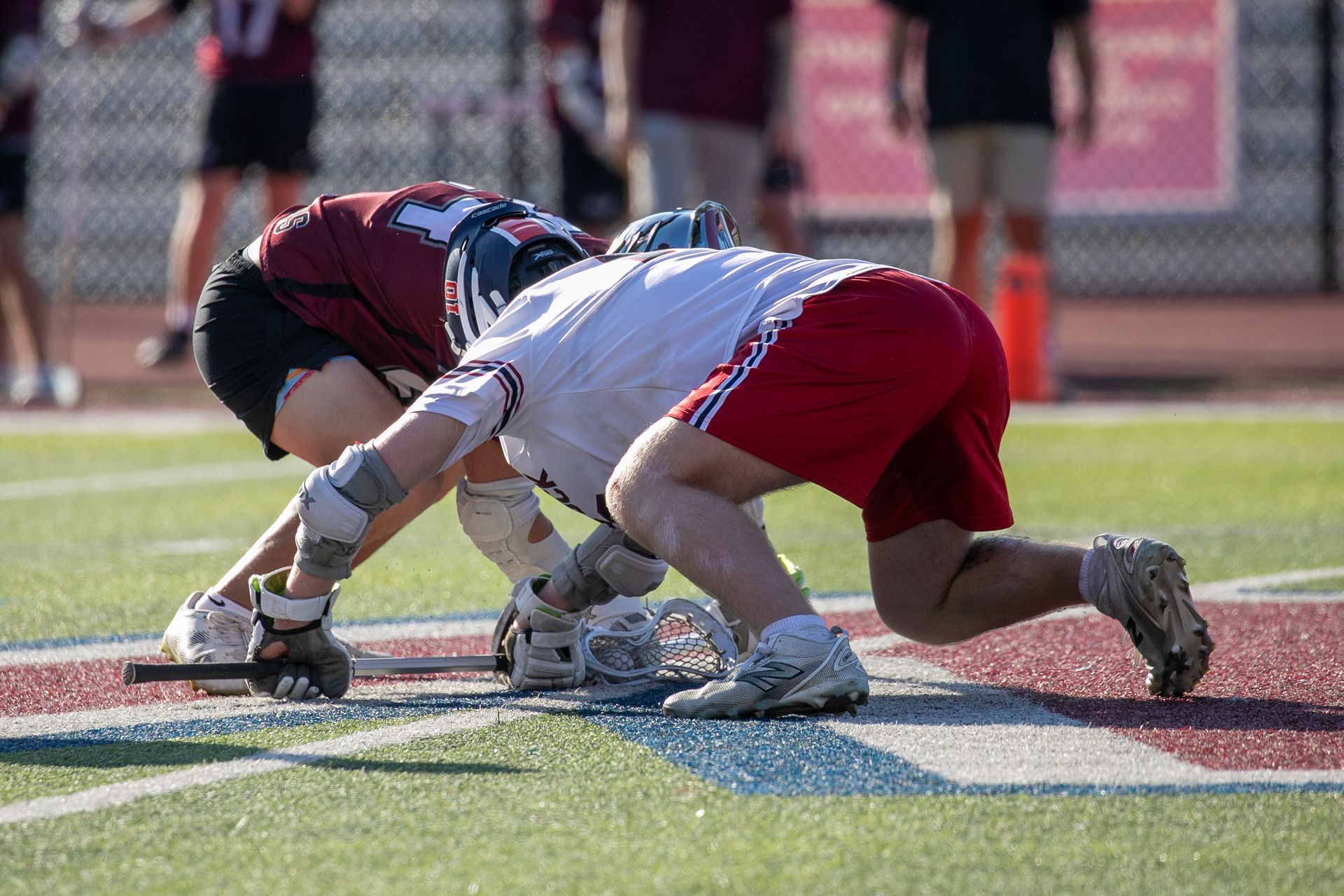 Two lacrosse players crouch at the faceoff line on a field.