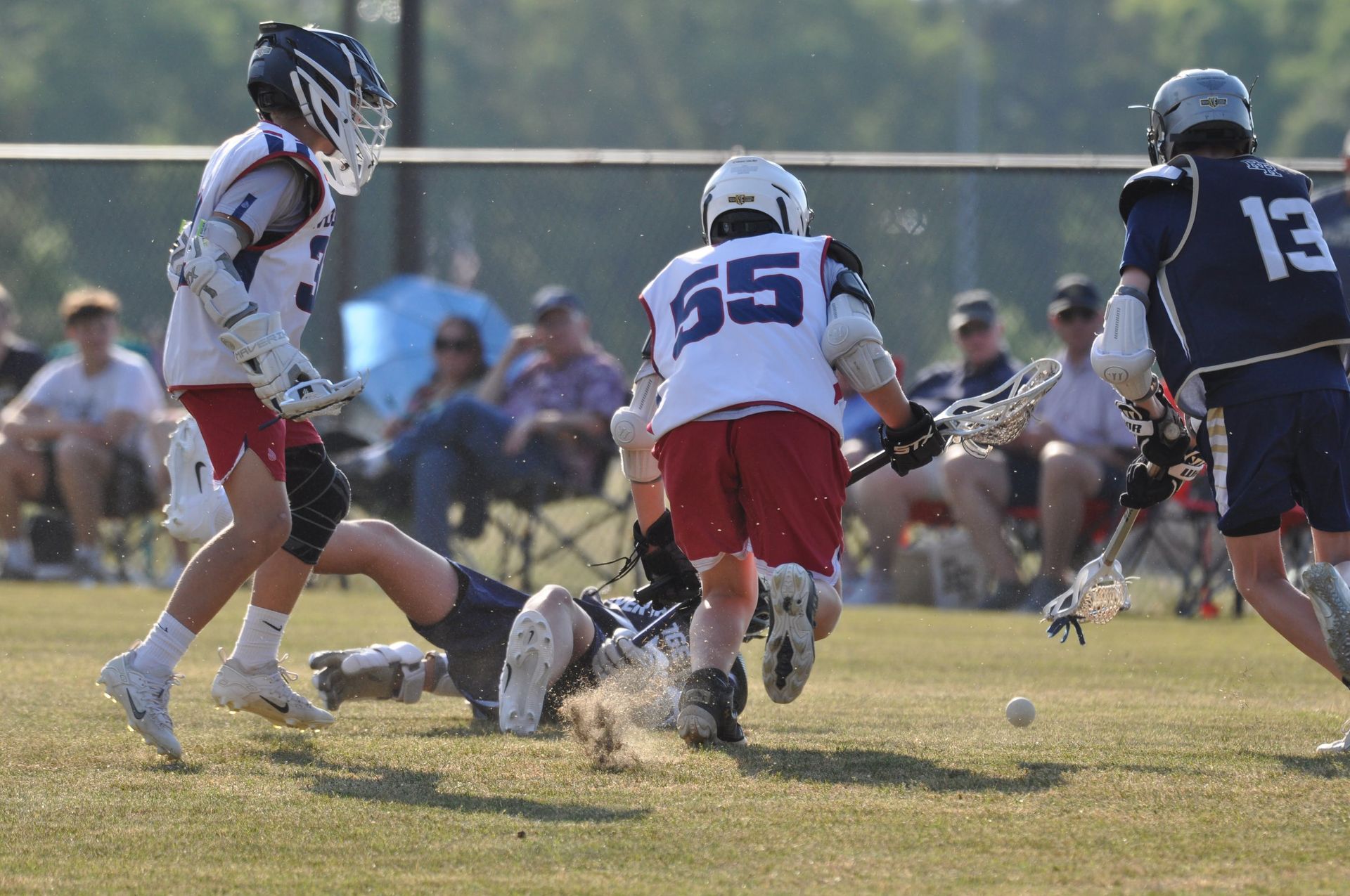 Lacrosse players in helmets and uniforms battle for the ball on a grassy field.