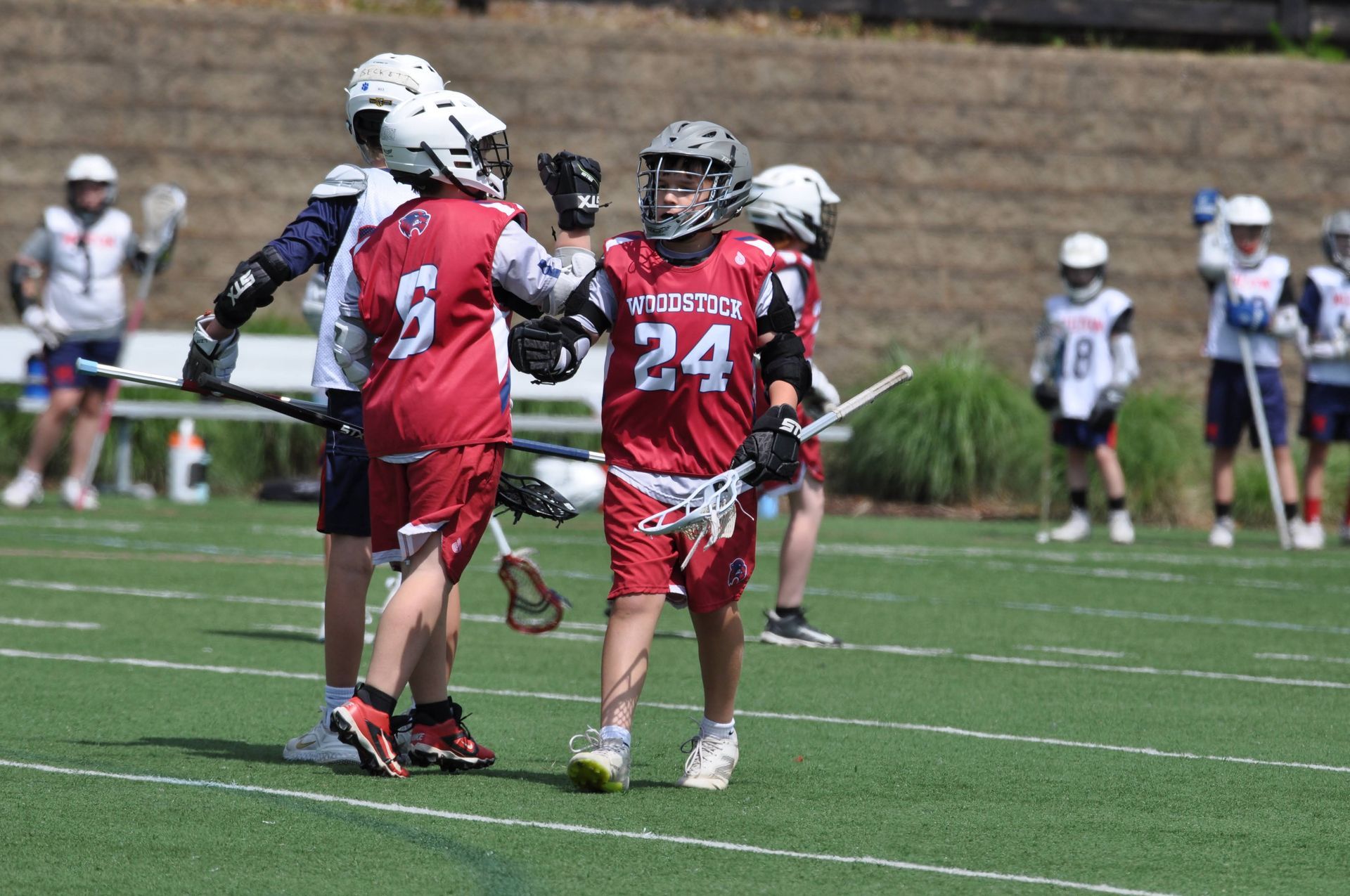 Three lacrosse players in red uniforms celebrating on a field during a game
