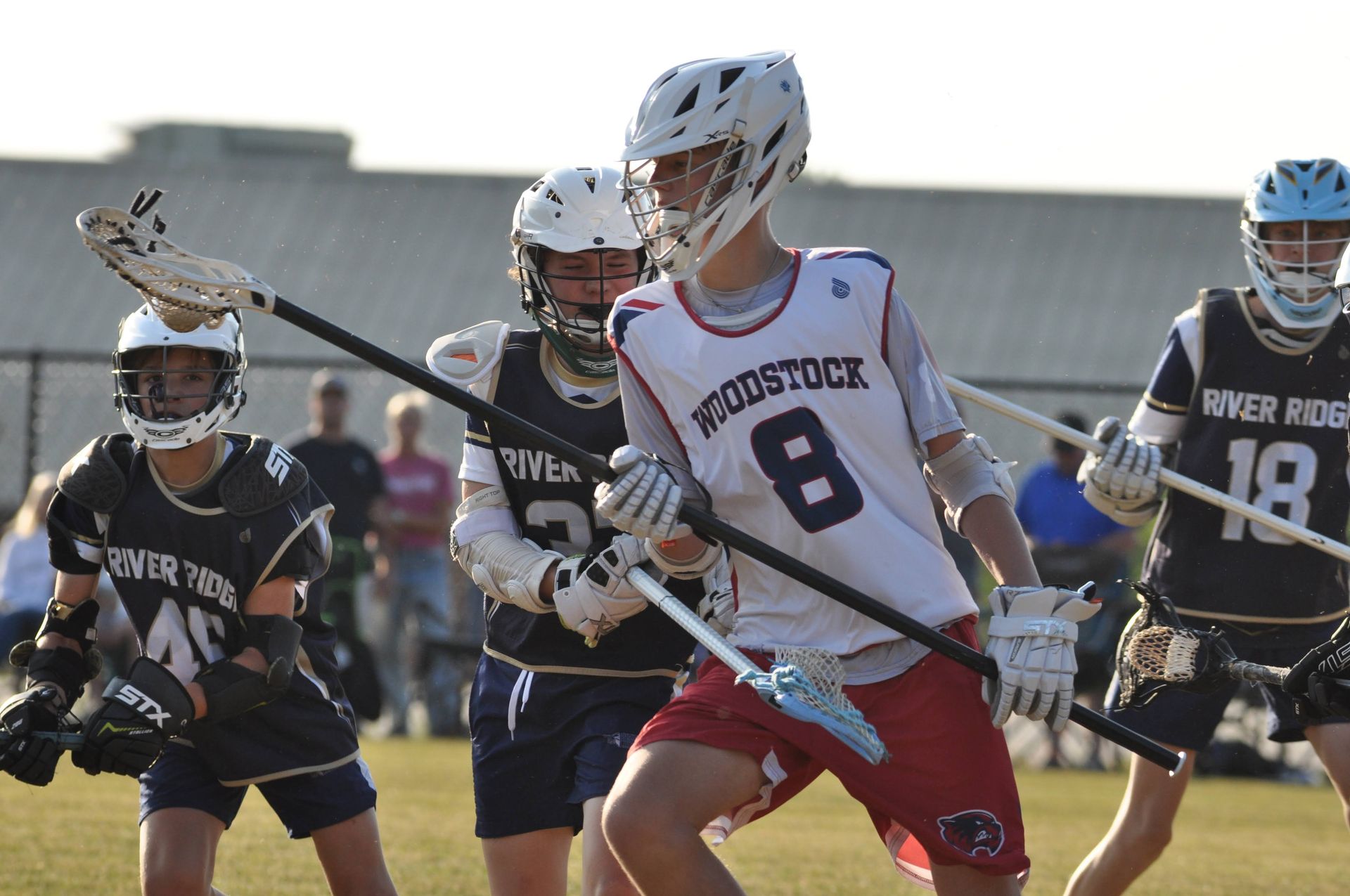 Field lacrosse players in white and dark uniforms compete for the ball outdoors.