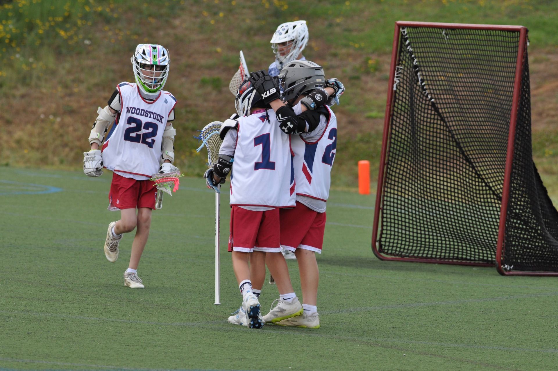 Lacrosse players in white and red uniforms celebrate near the goal on a grassy field.