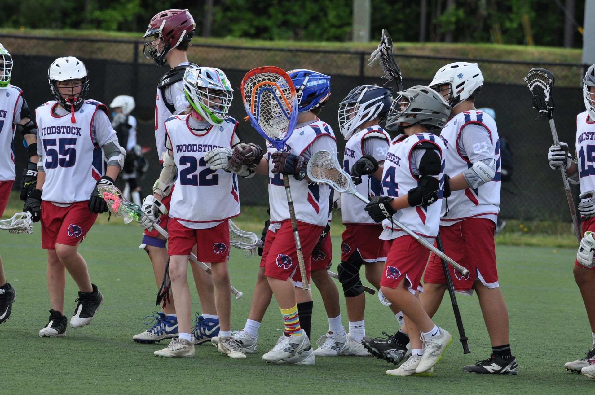 Youth lacrosse team in white and red uniforms huddles on the field during a game