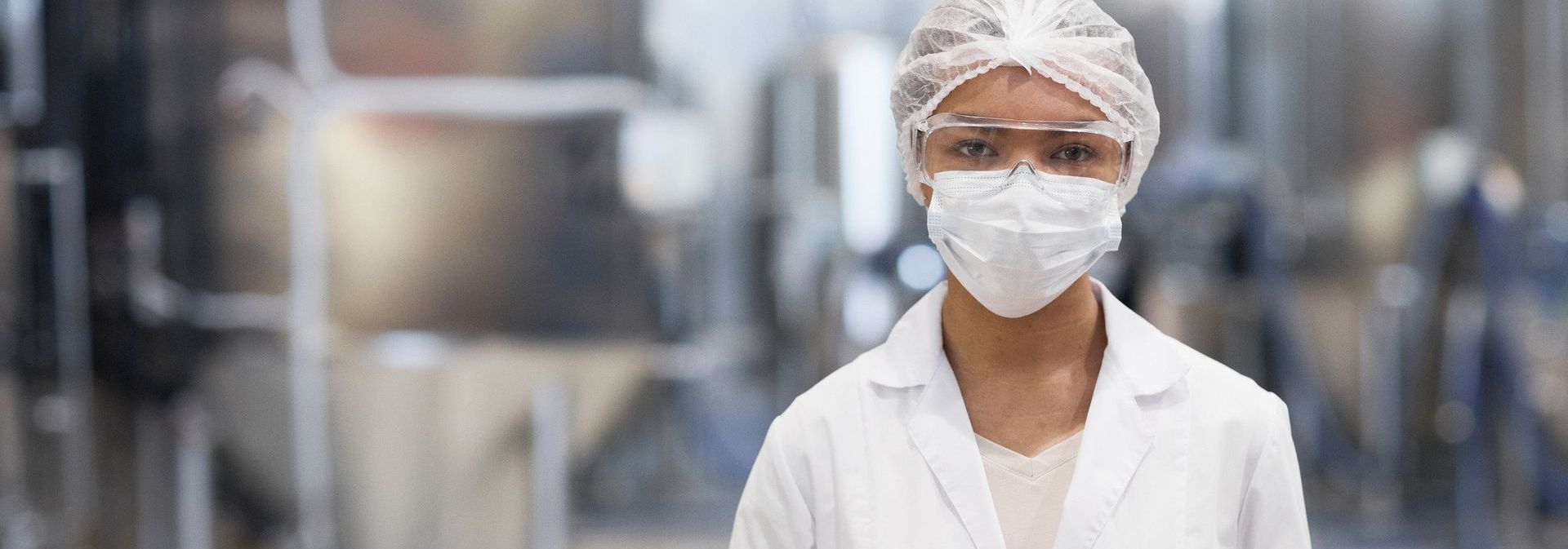 A woman wearing a mask and gloves is holding a tablet in a factory