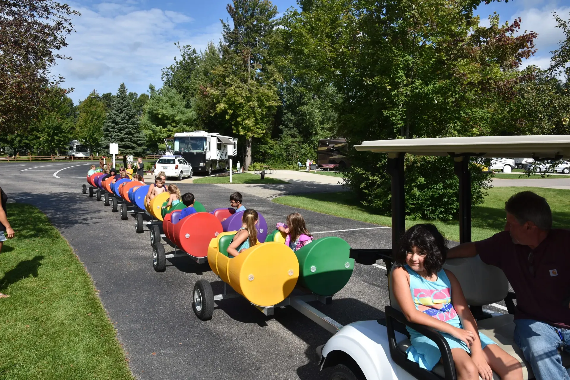 A group of children are riding a colorful train on a golf cart.
