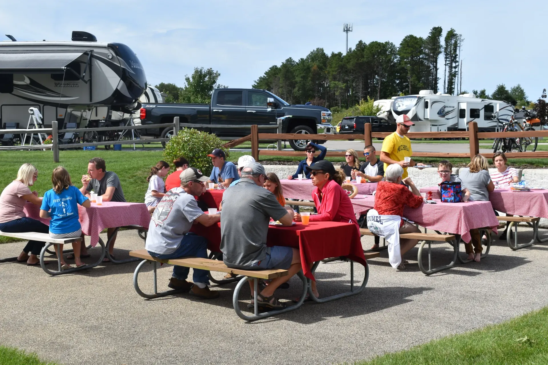 A group of people are sitting at picnic tables in a park.