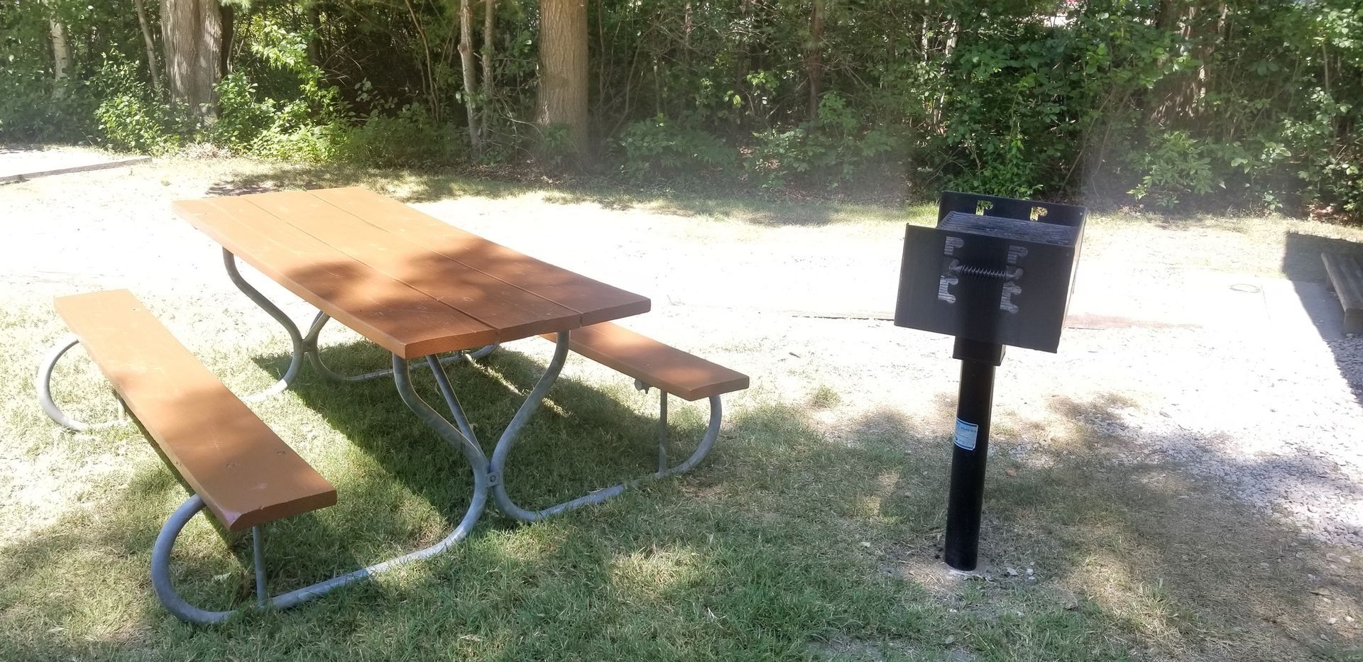 A picnic table with two benches and a grill in the grass.