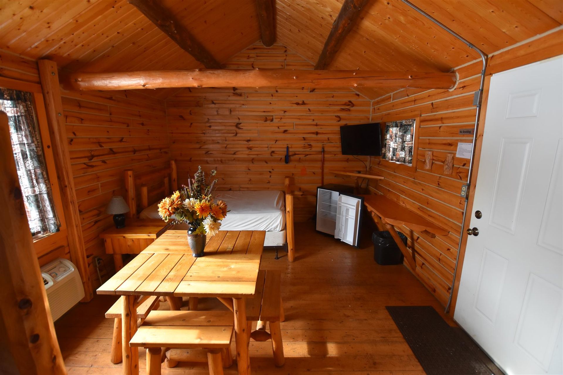 A wooden cabin with a table and benches and a bed.