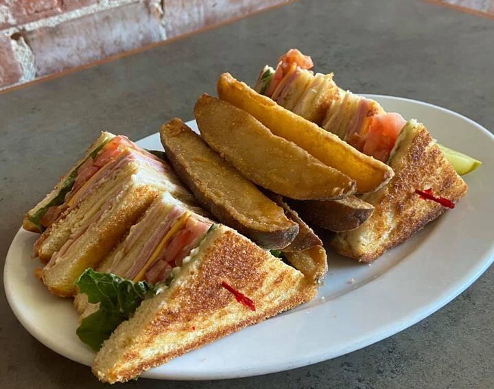 A white plate topped with a club sandwich and potato wedges