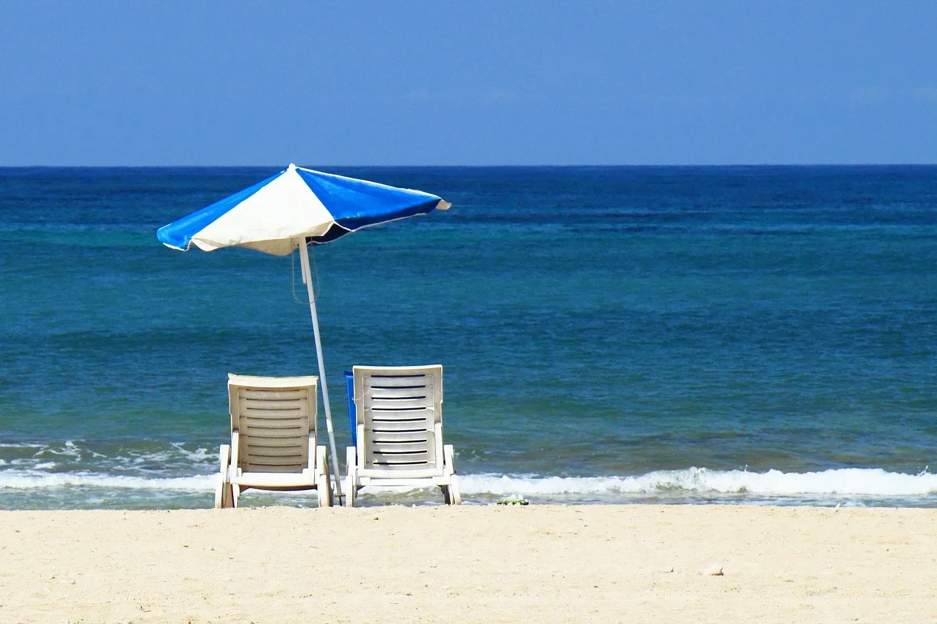 Two chairs under a blue and white umbrella on a beach