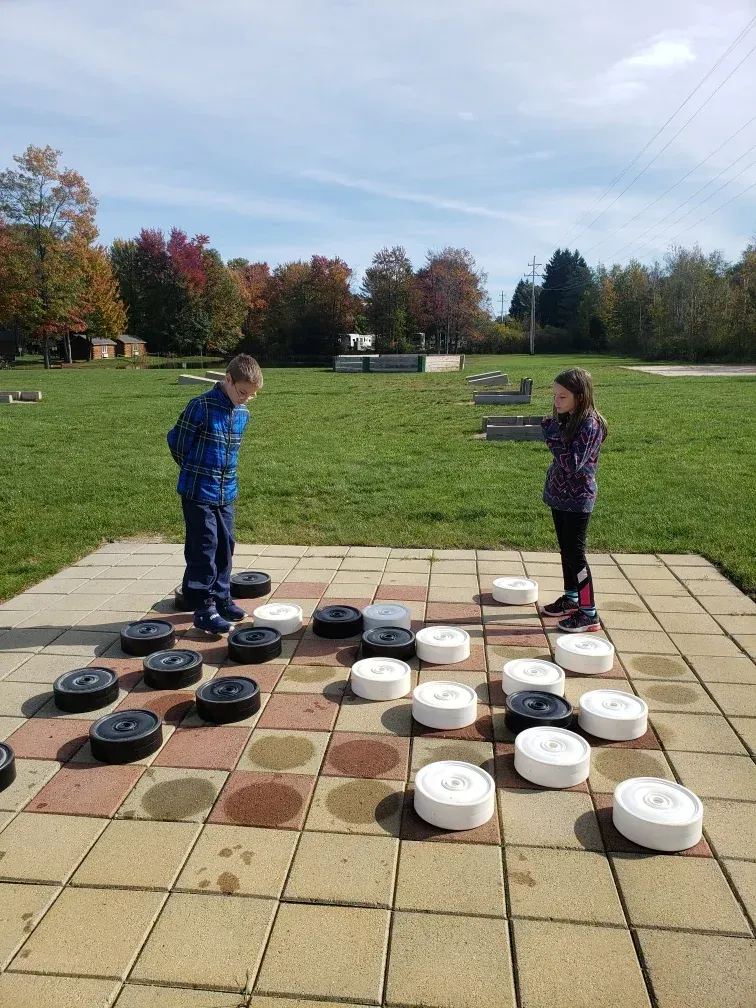 A boy and a girl are playing a game of checkers on a patio.