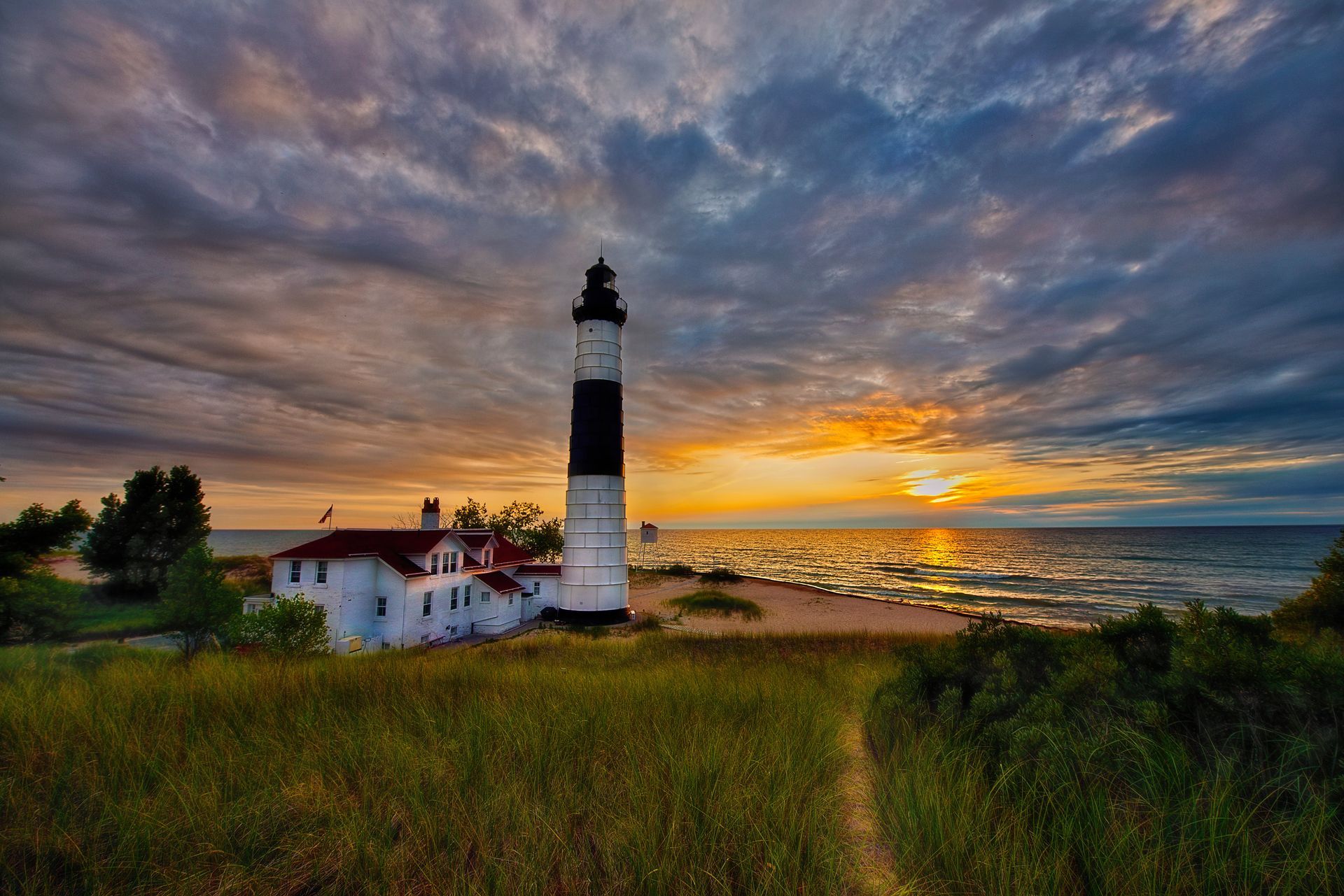 A lighthouse is sitting on top of a grassy hill next to the ocean at sunset.