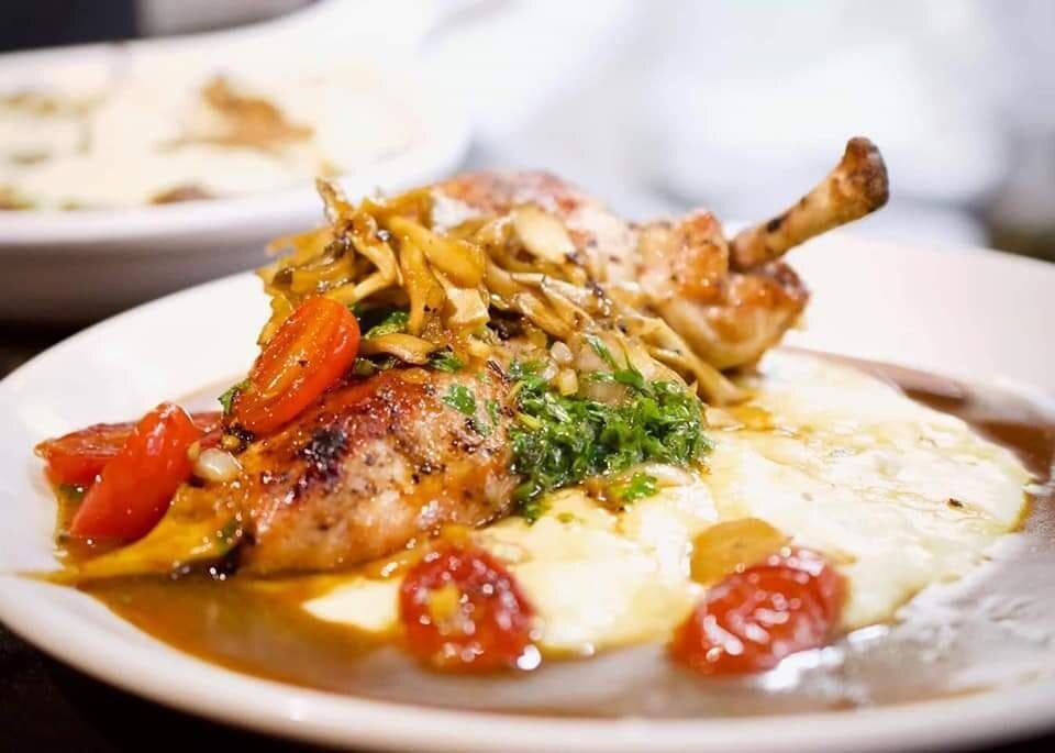 A close up of a plate of food with meat , mashed potatoes and tomatoes on a table.