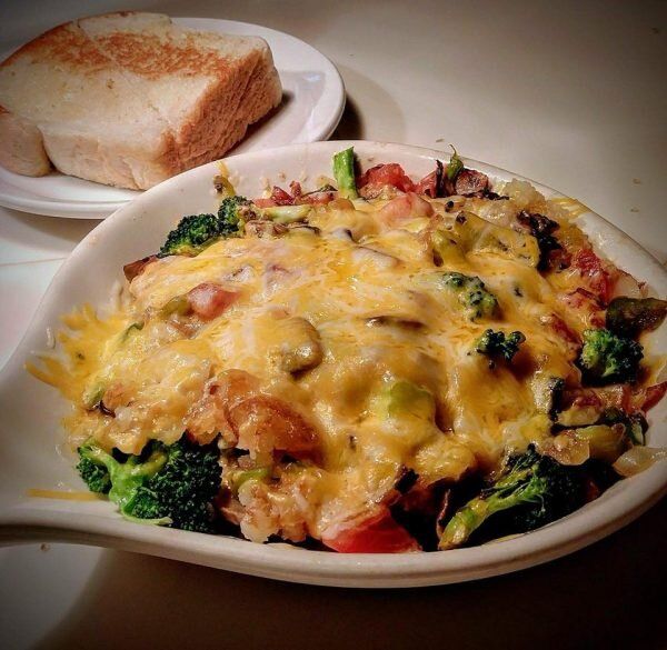 A bowl of food with broccoli and cheese next to a plate of bread