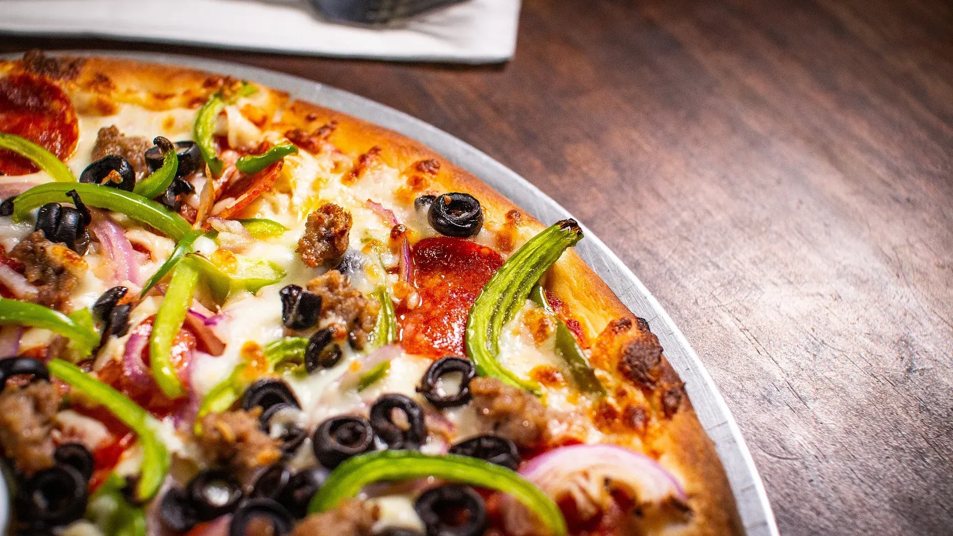 A pizza with pepperoni , olives , peppers , onions and cheese is sitting on a wooden table.
