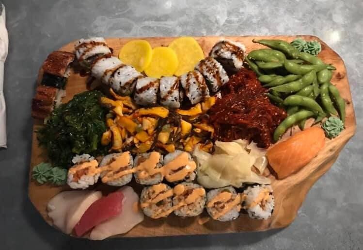 A wooden cutting board topped with a variety of sushi and vegetables.