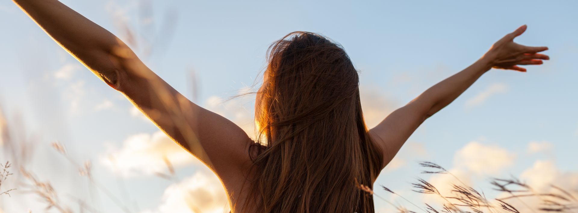 A woman is standing in a field with her arms outstretched.