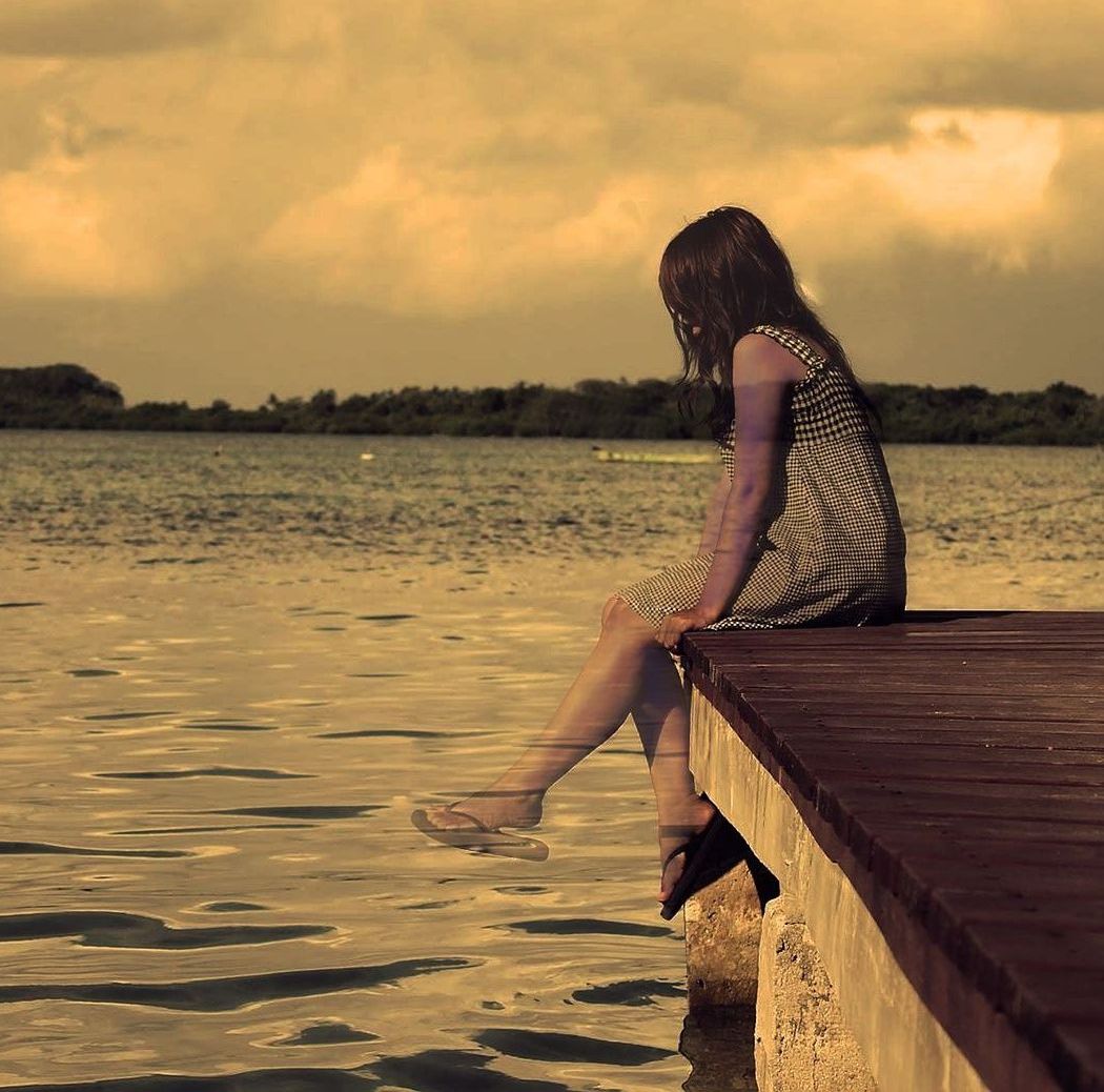 A woman is sitting on a dock overlooking a body of water