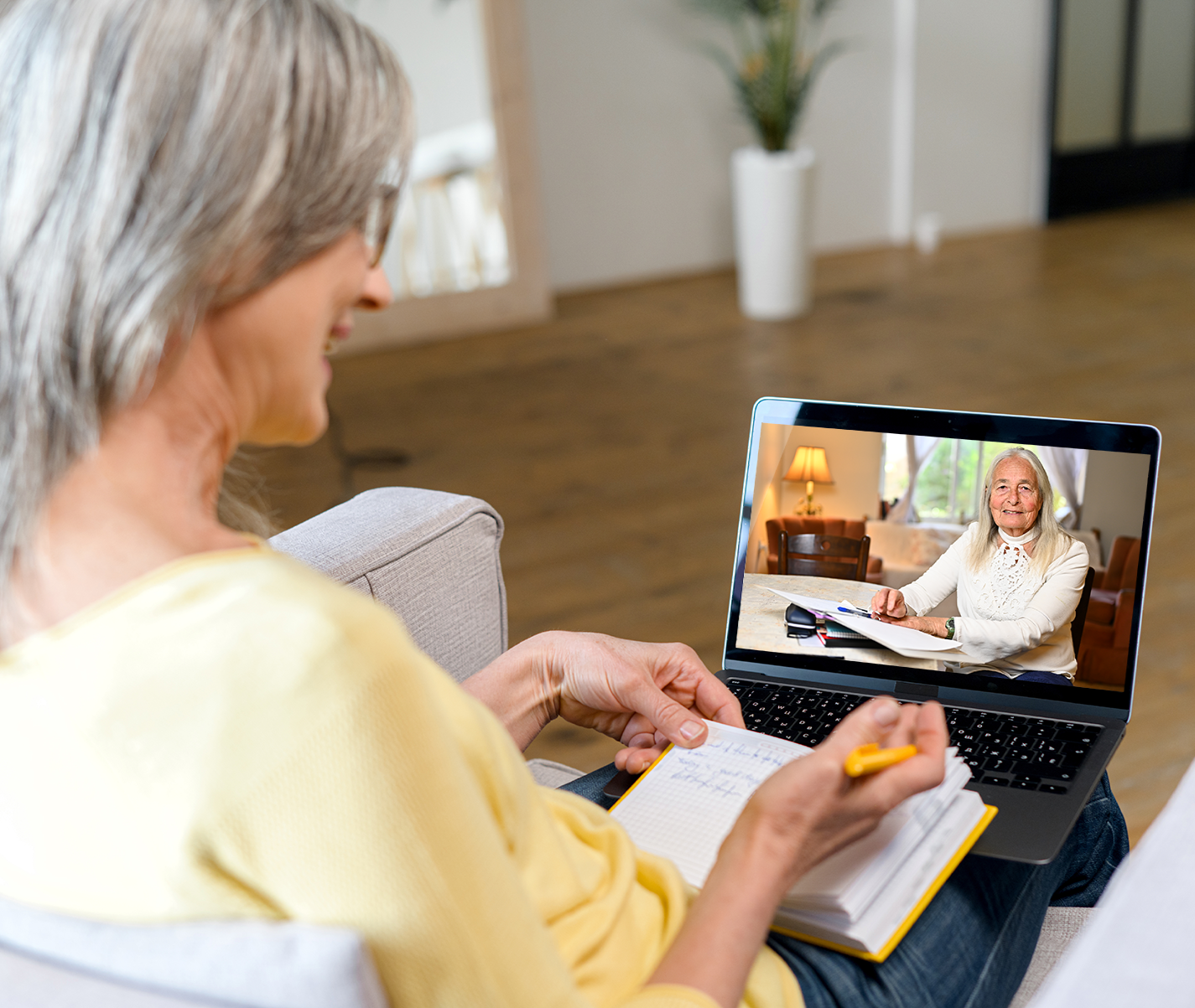 An older woman is sitting on a couch using a laptop computer.