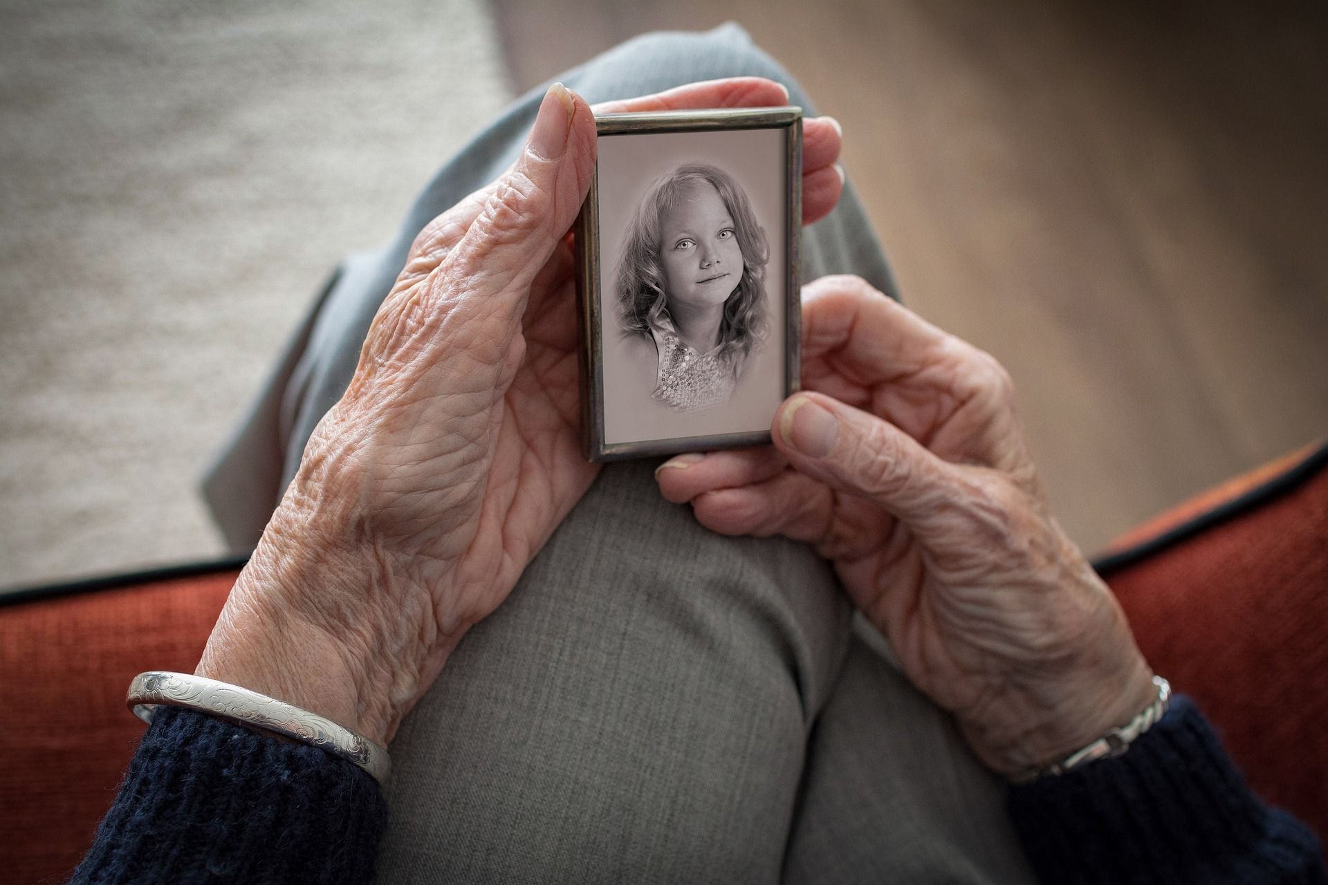 An elderly woman is holding a black and white photo of a young girl.