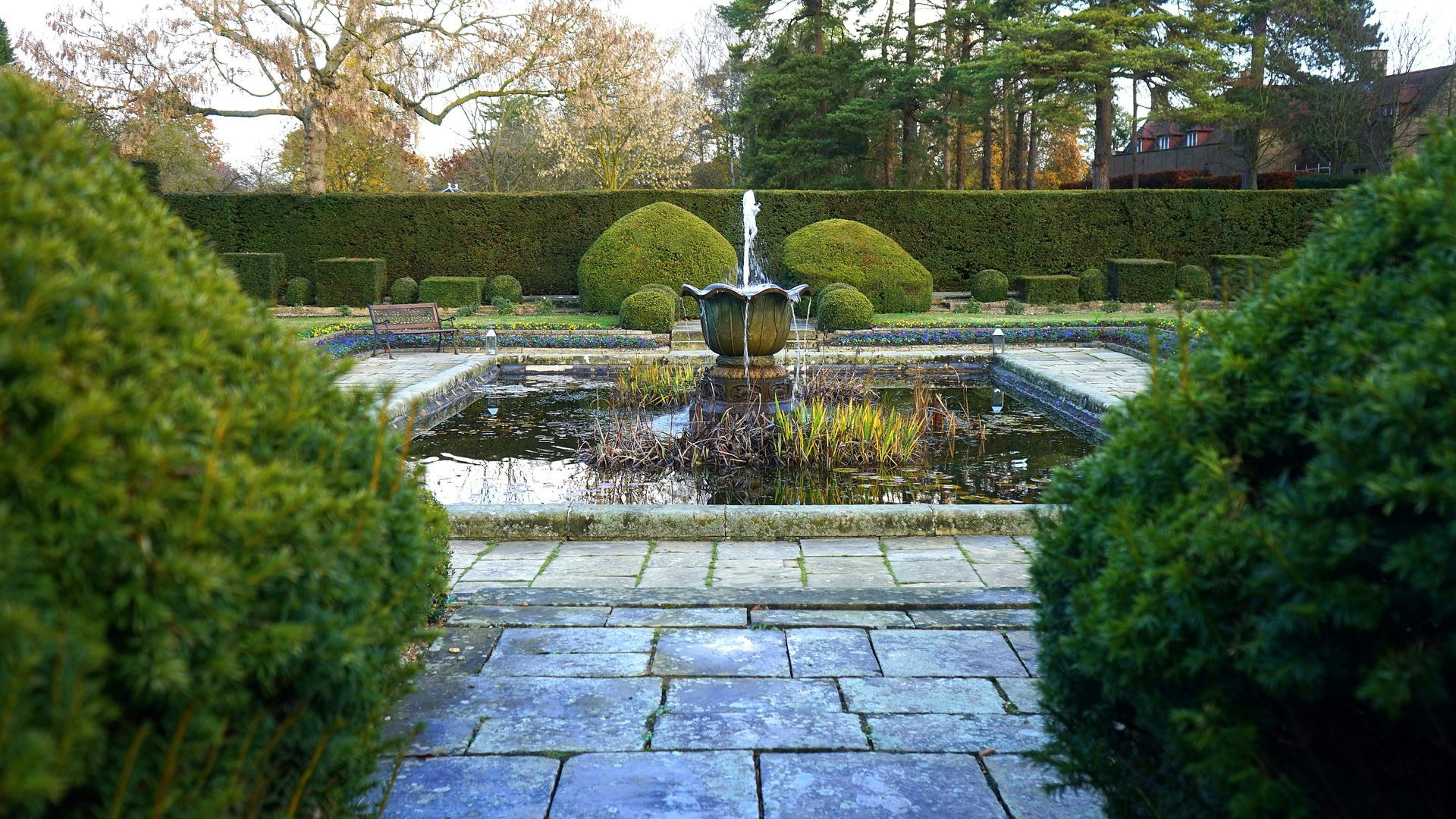 Fountain in a formal garden, with pond, hedges, and trees.