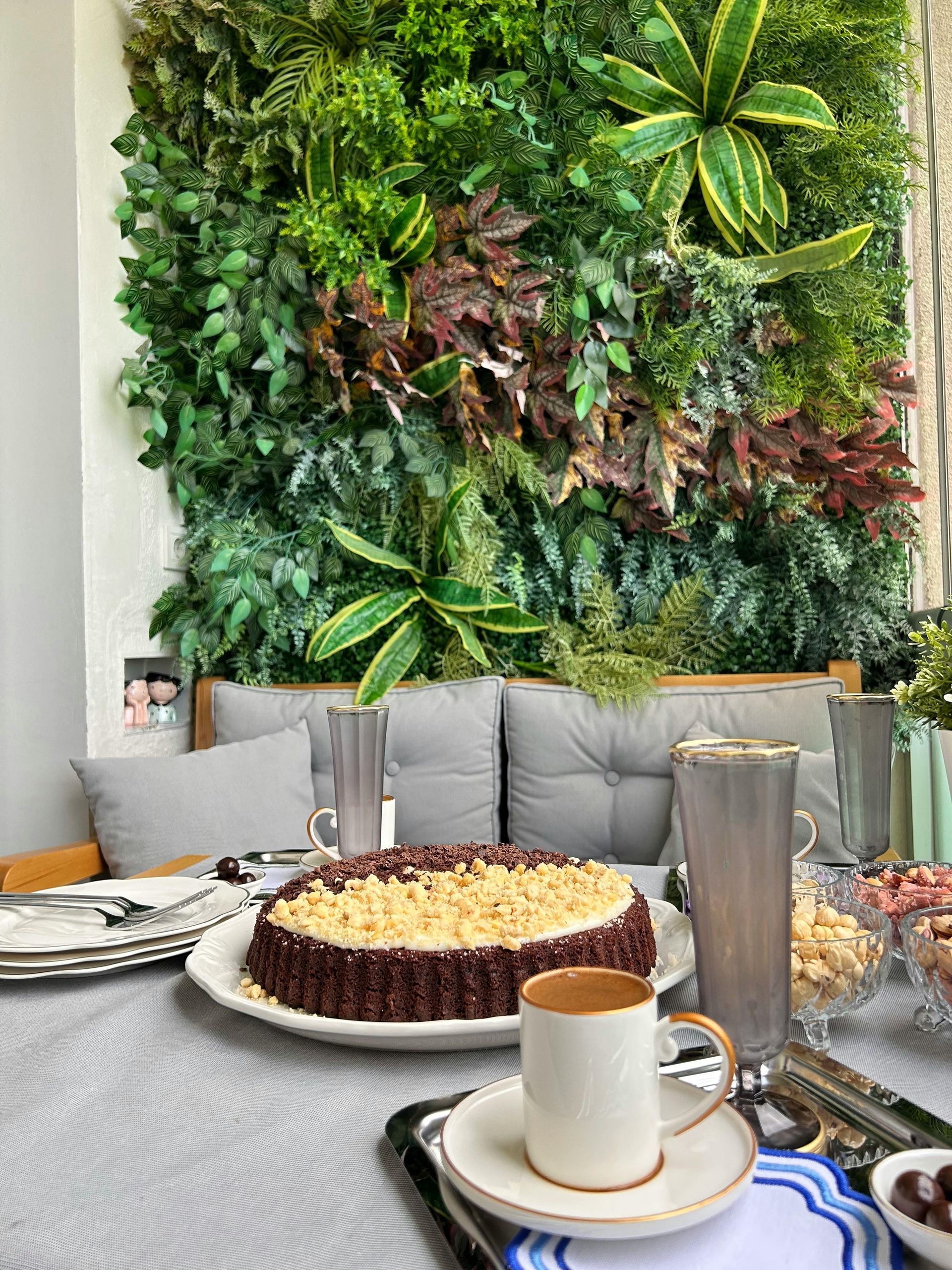 A table set with a cake, coffee, and dishes in front of a living wall.