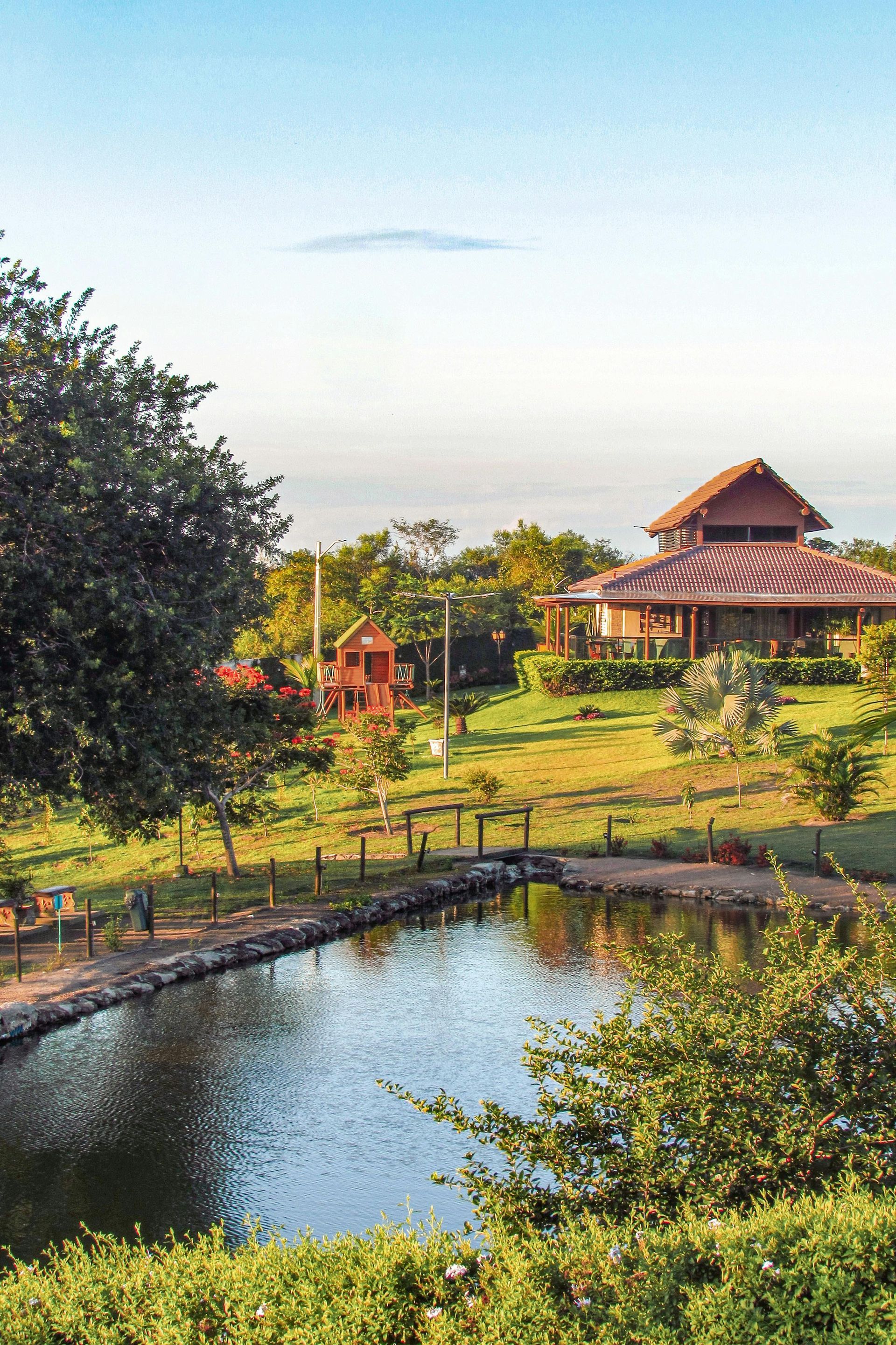Tranquil pond beside a rustic pavilion and trees under a clear sky