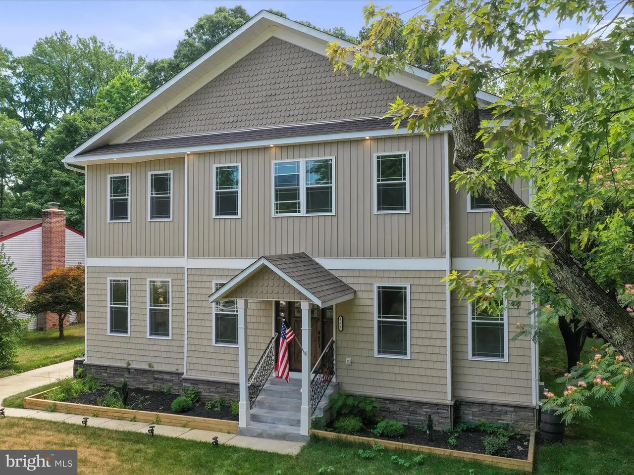 Two-story beige house with multiple windows, small porch, and green landscaping.