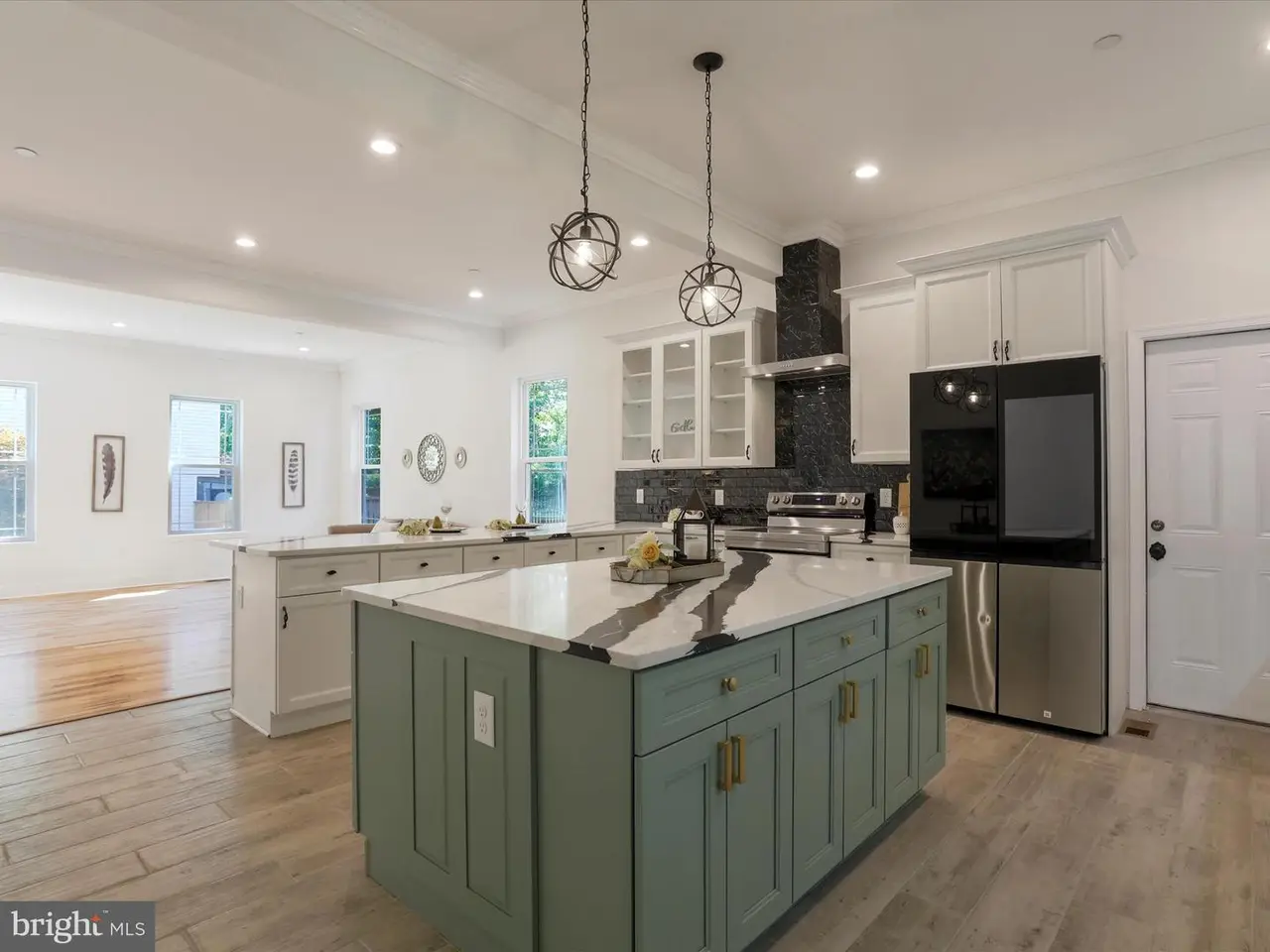 Spacious kitchen with a green island, white cabinets, stainless steel appliances, and pendant lights.