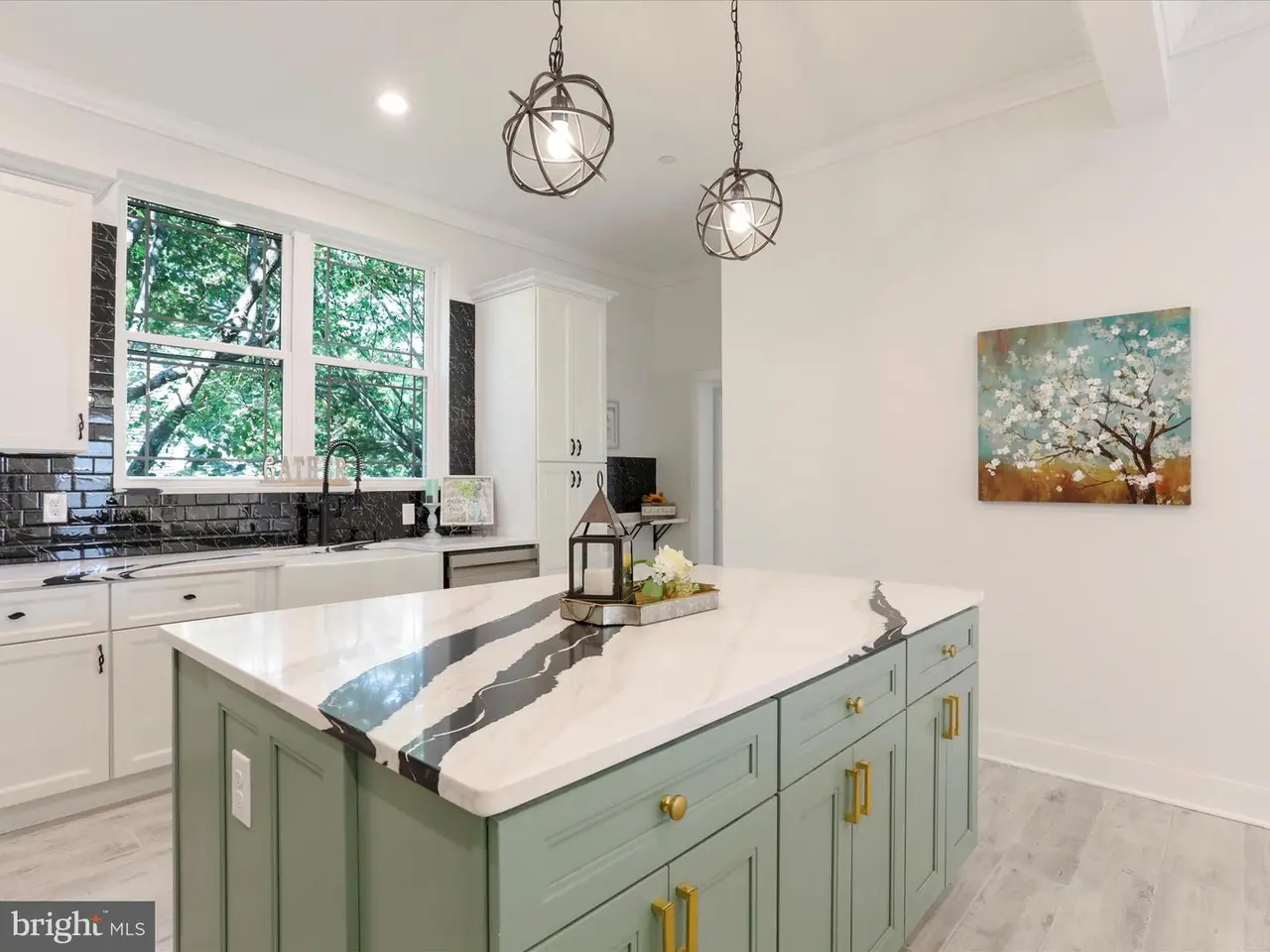 Kitchen with sage green island, white countertops with black veining, white cabinets, and two pendant lights.