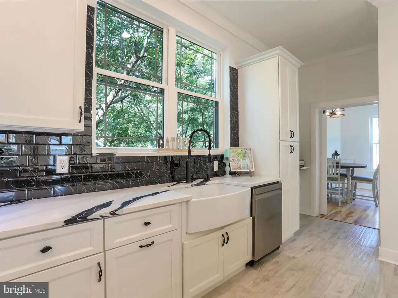 White kitchen with black backsplash and countertop, stainless steel appliances, and a window.