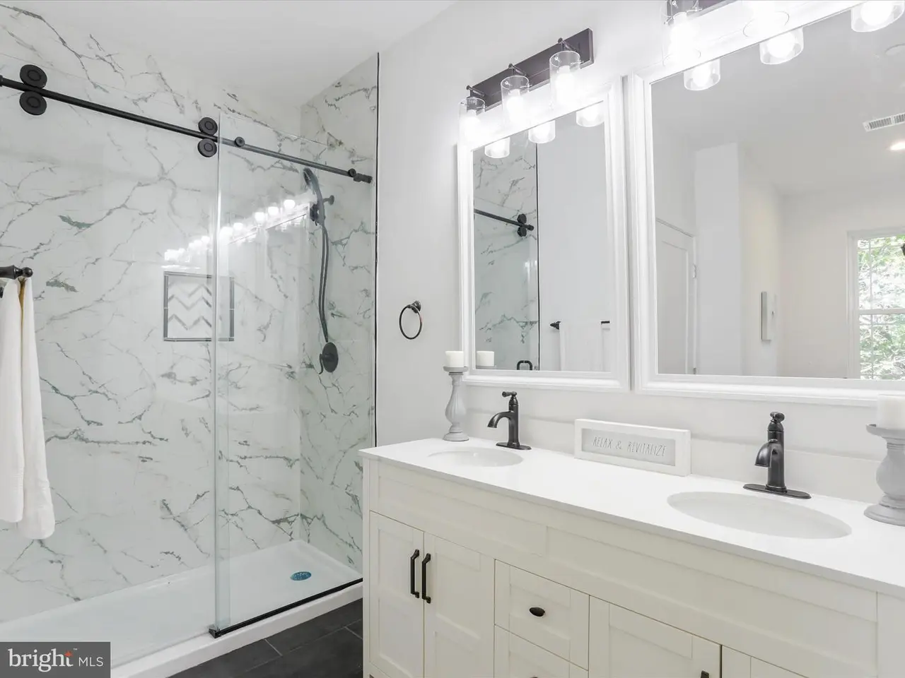 Modern white bathroom with marble shower, double vanity, and black accents.