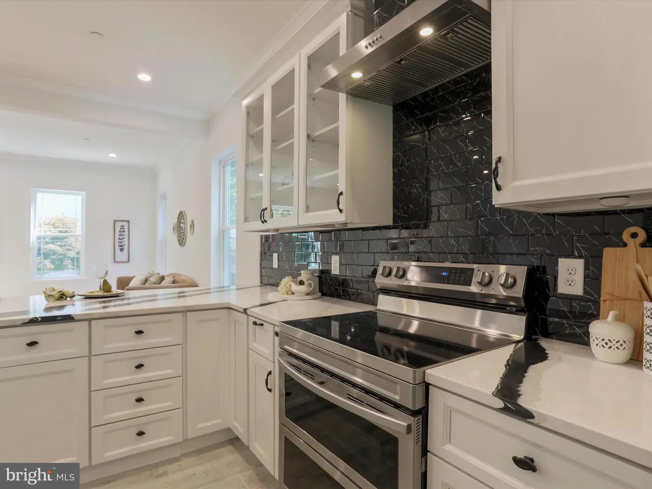 Modern white kitchen with stainless steel appliances, black tile backsplash, and white cabinets.