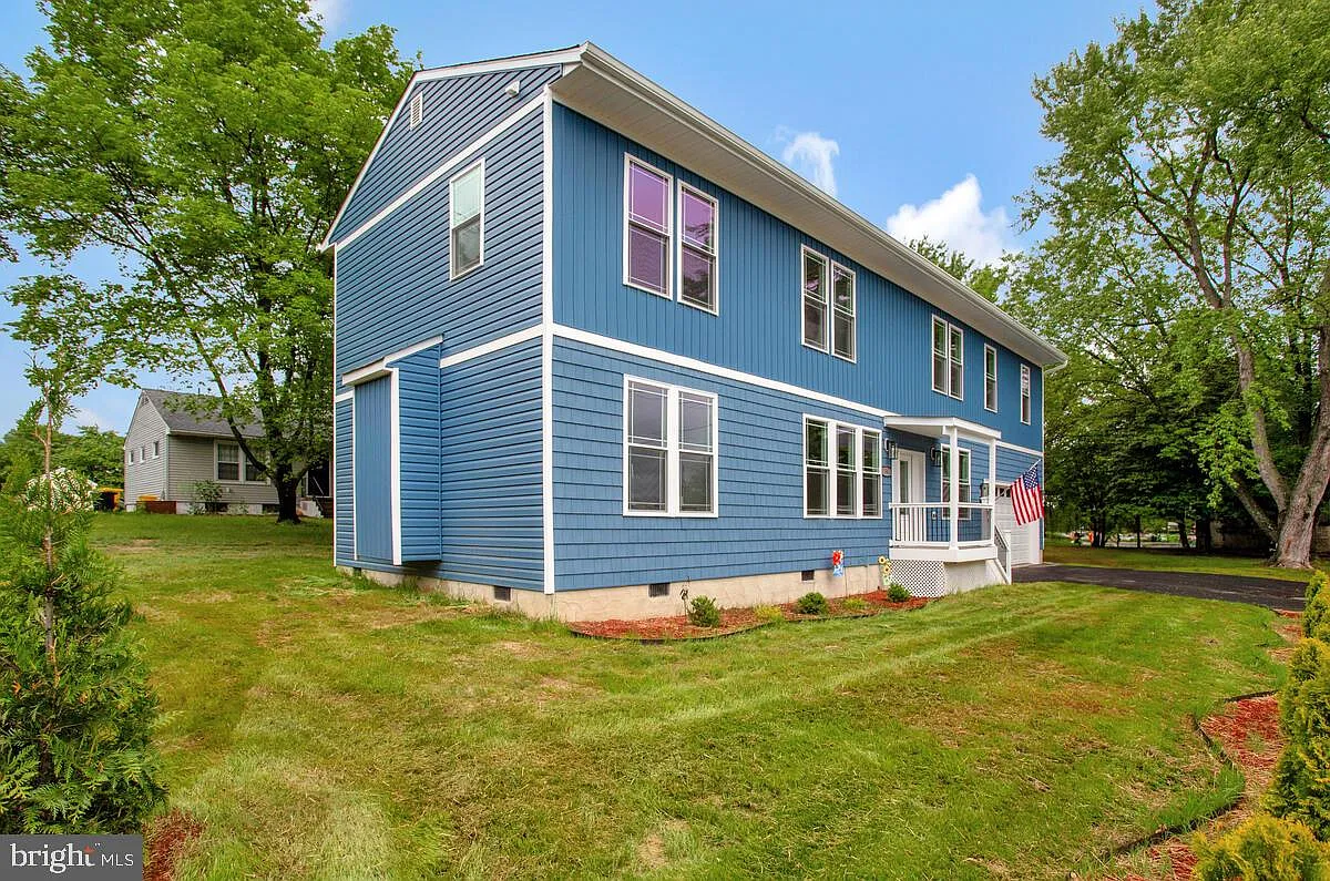 Blue two-story house with white trim and a small front porch, surrounded by green grass and trees.