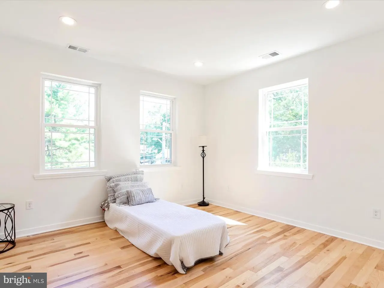 Empty, sunlit room with hardwood floors, three windows, and a chaise lounge.
