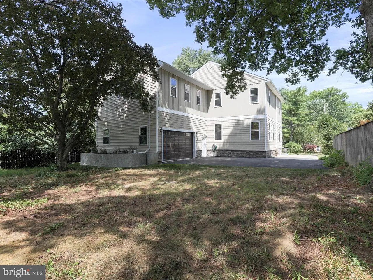 Back view of a multi-story, light-colored house with a dark garage door, set on a grassy lot.
