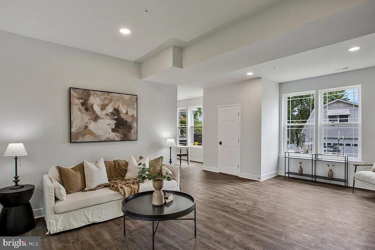 Living room with cream-colored sofa, dark coffee table, large windows, and hardwood floors.