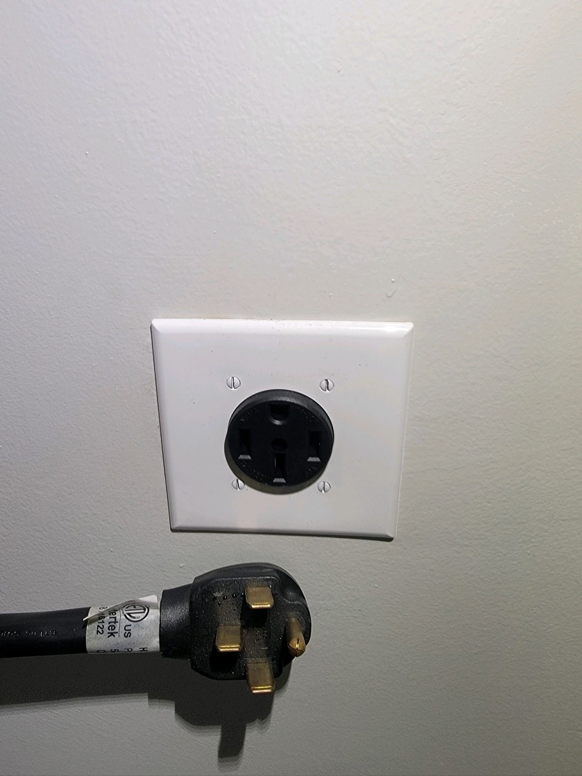Wall outlet with a black plug and exposed cable against a light-colored wall.
