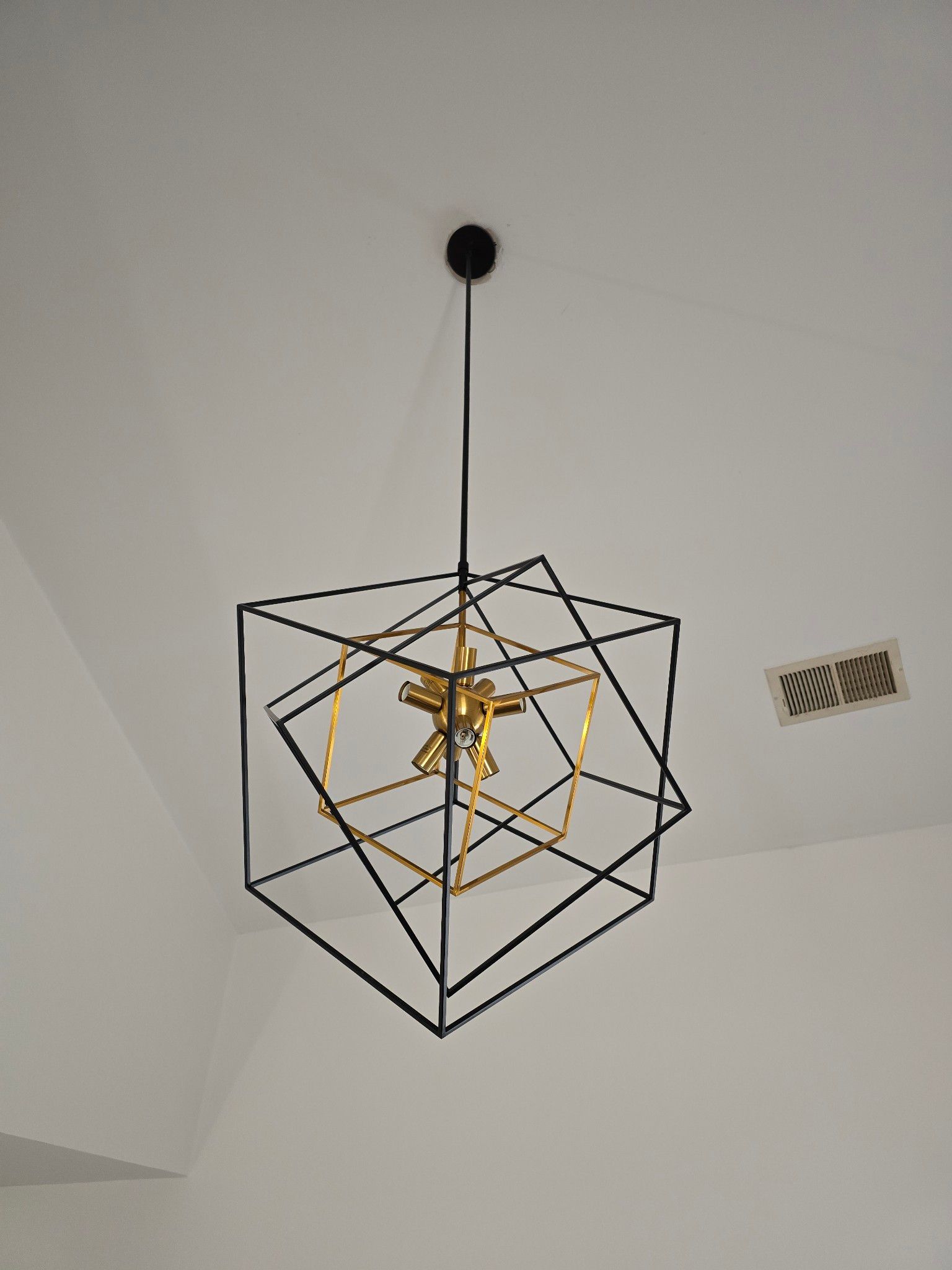 Modern geometric black wire pendant light with gold center hanging from the ceiling