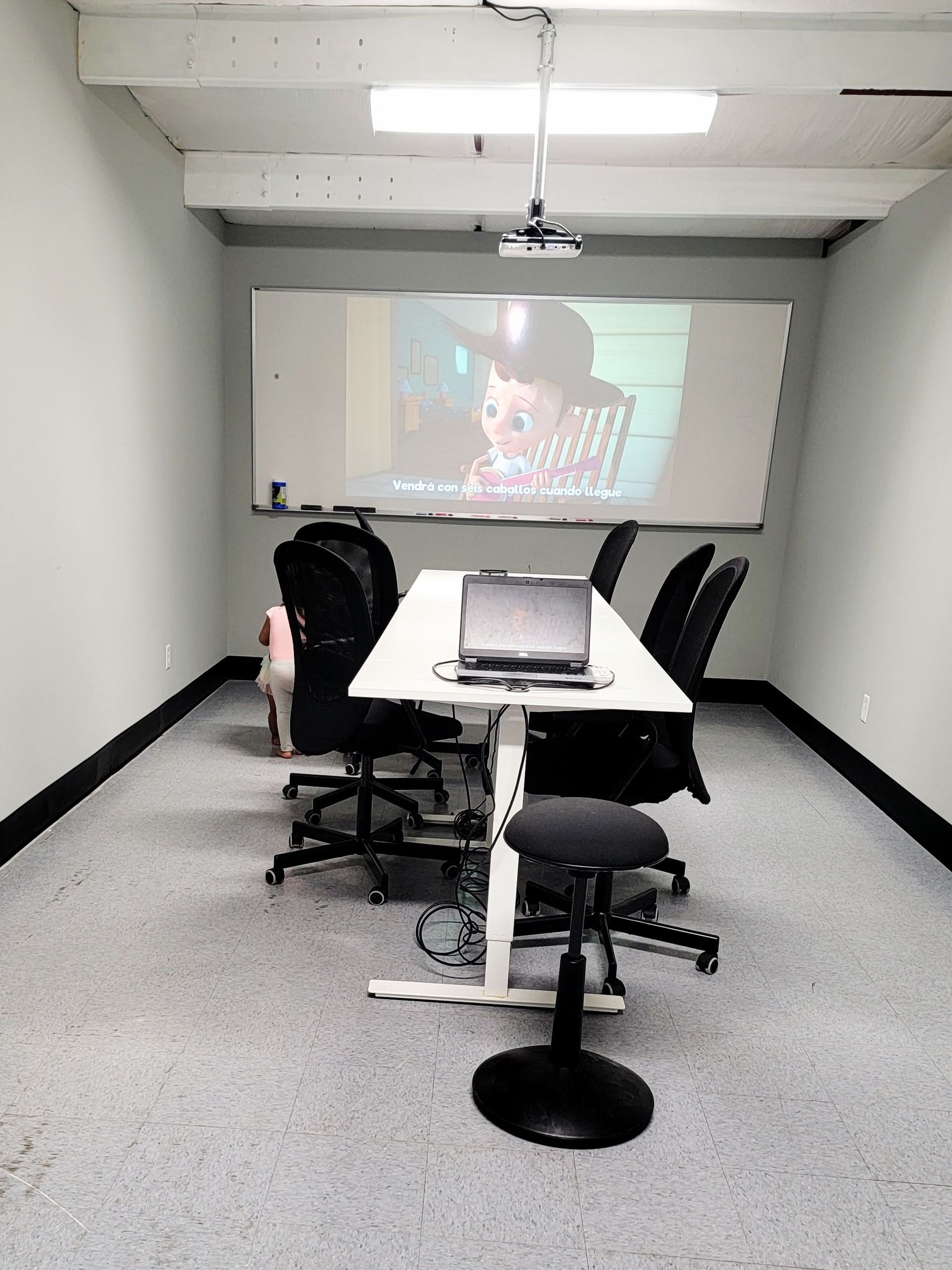 Small meeting room with projector screen, white table, and office chairs