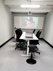 Small meeting room with a projector screen showing a video and a laptop on the conference table.