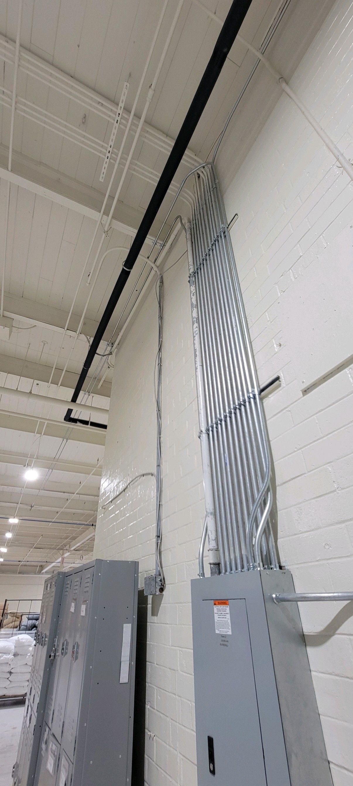 Industrial interior with electrical panels and bundled cables running up a white wall to the ceiling