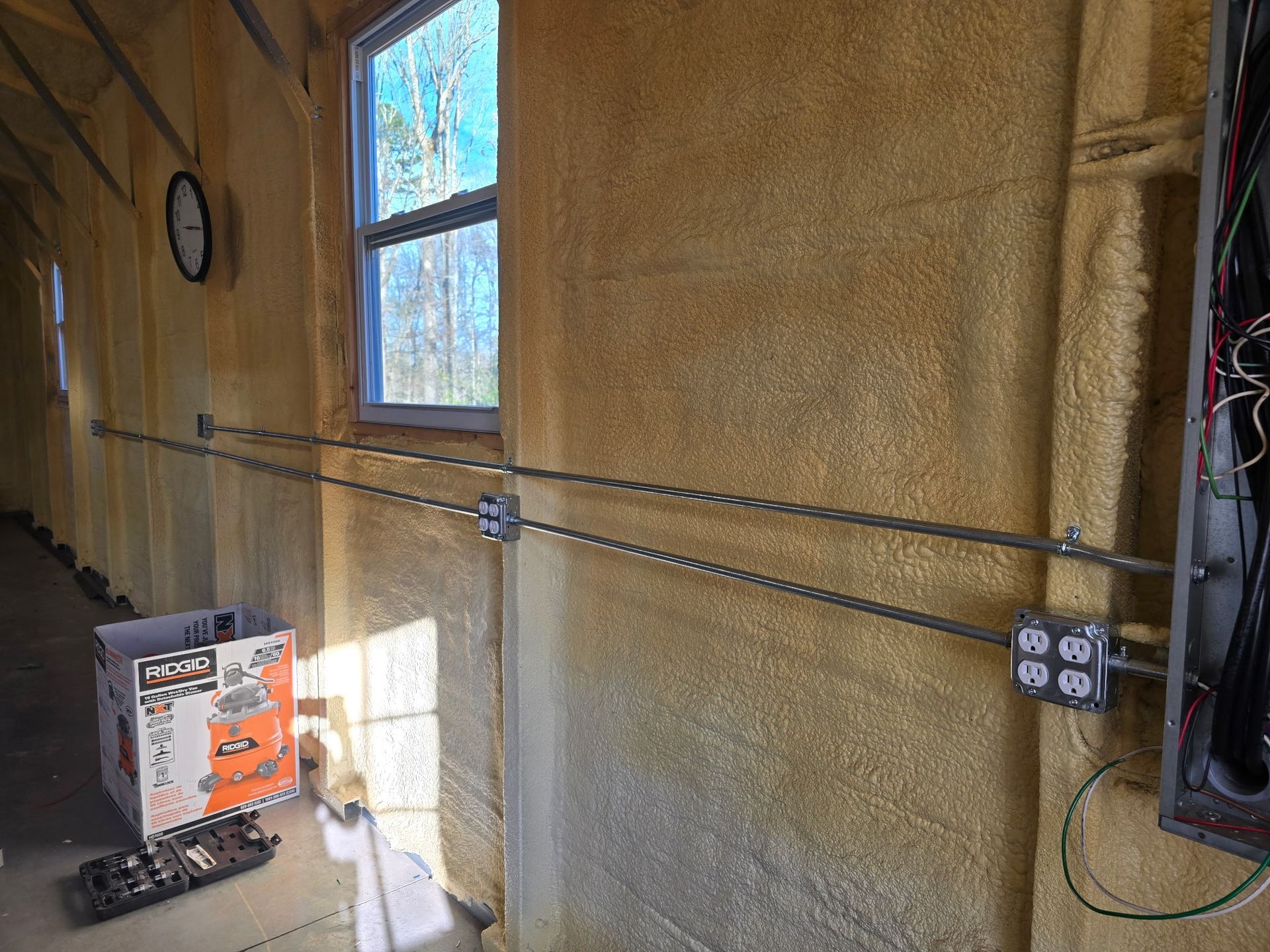 Insulated wall with exposed electrical wiring, outlet boxes, and a window in a construction site