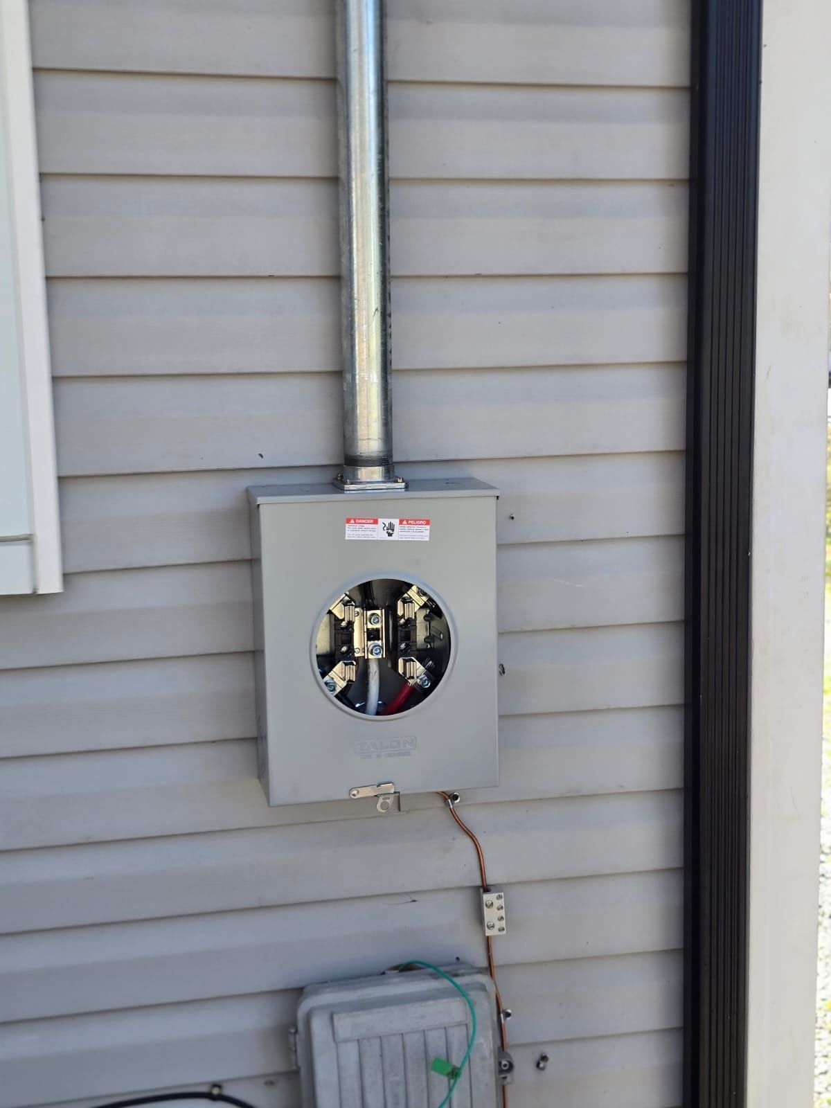 Gray electrical meter box and conduit mounted on a house exterior wall.