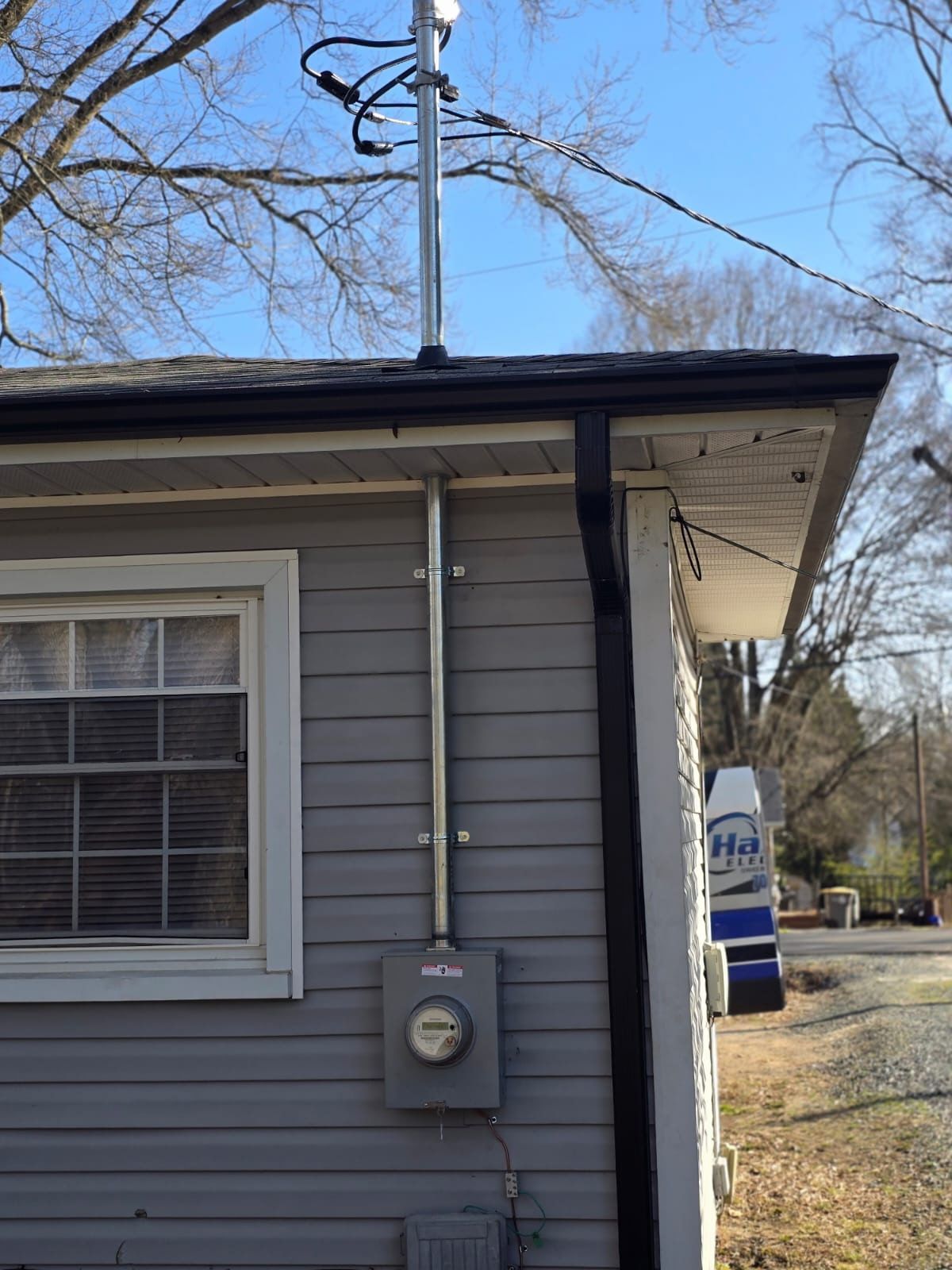 Gray house side with window, utility meter, and electrical lines under a blue sky