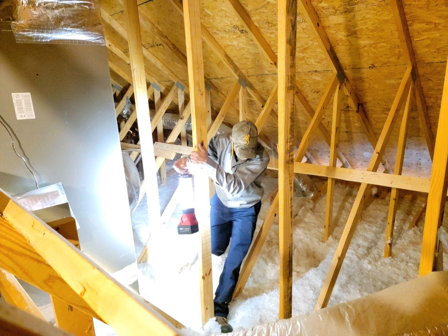 Person inspecting attic framing with a flashlight beside exposed wooden beams and insulation.