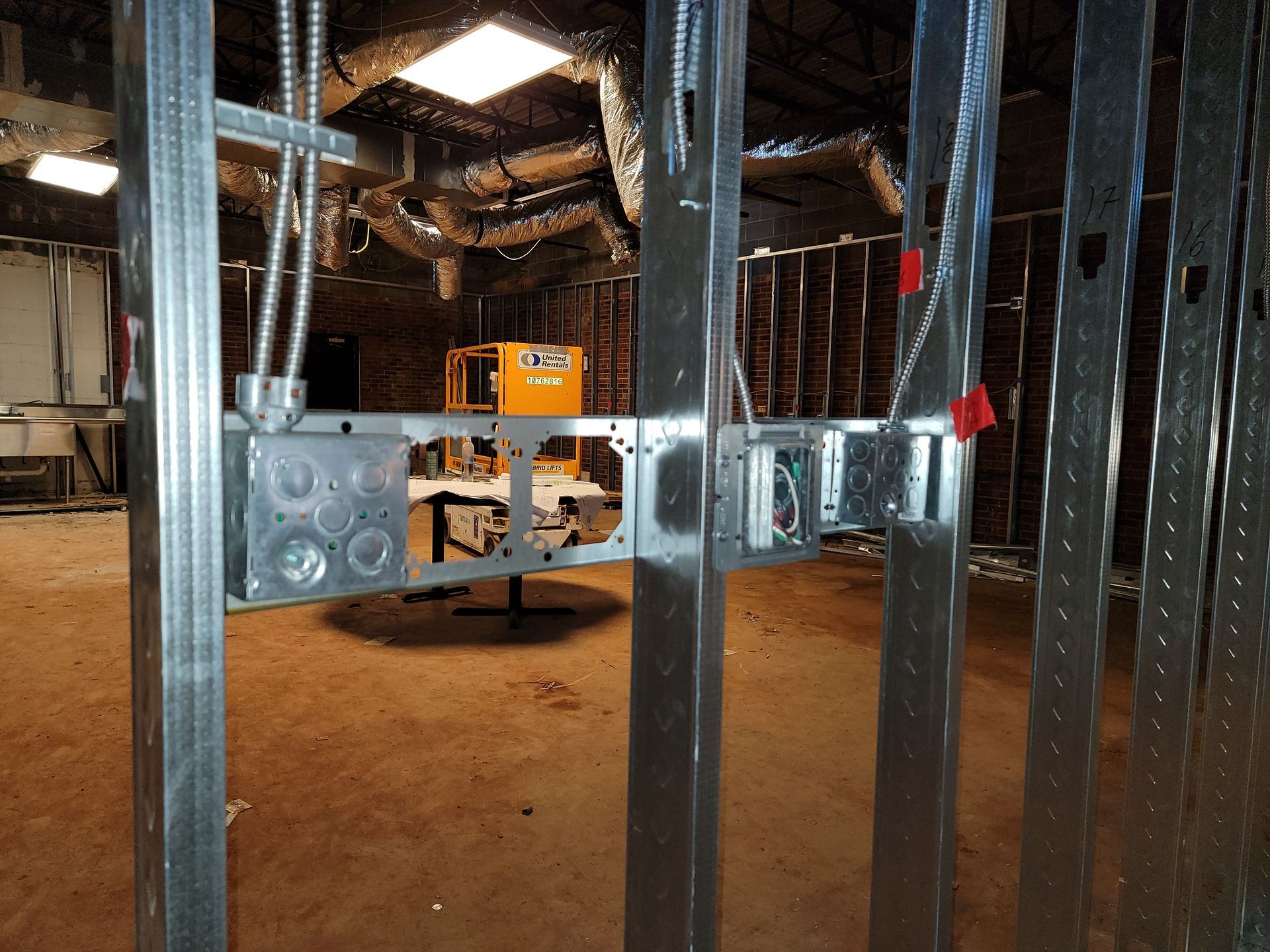 Exposed metal framing and ductwork inside a construction site, with a yellow machine in the background.
