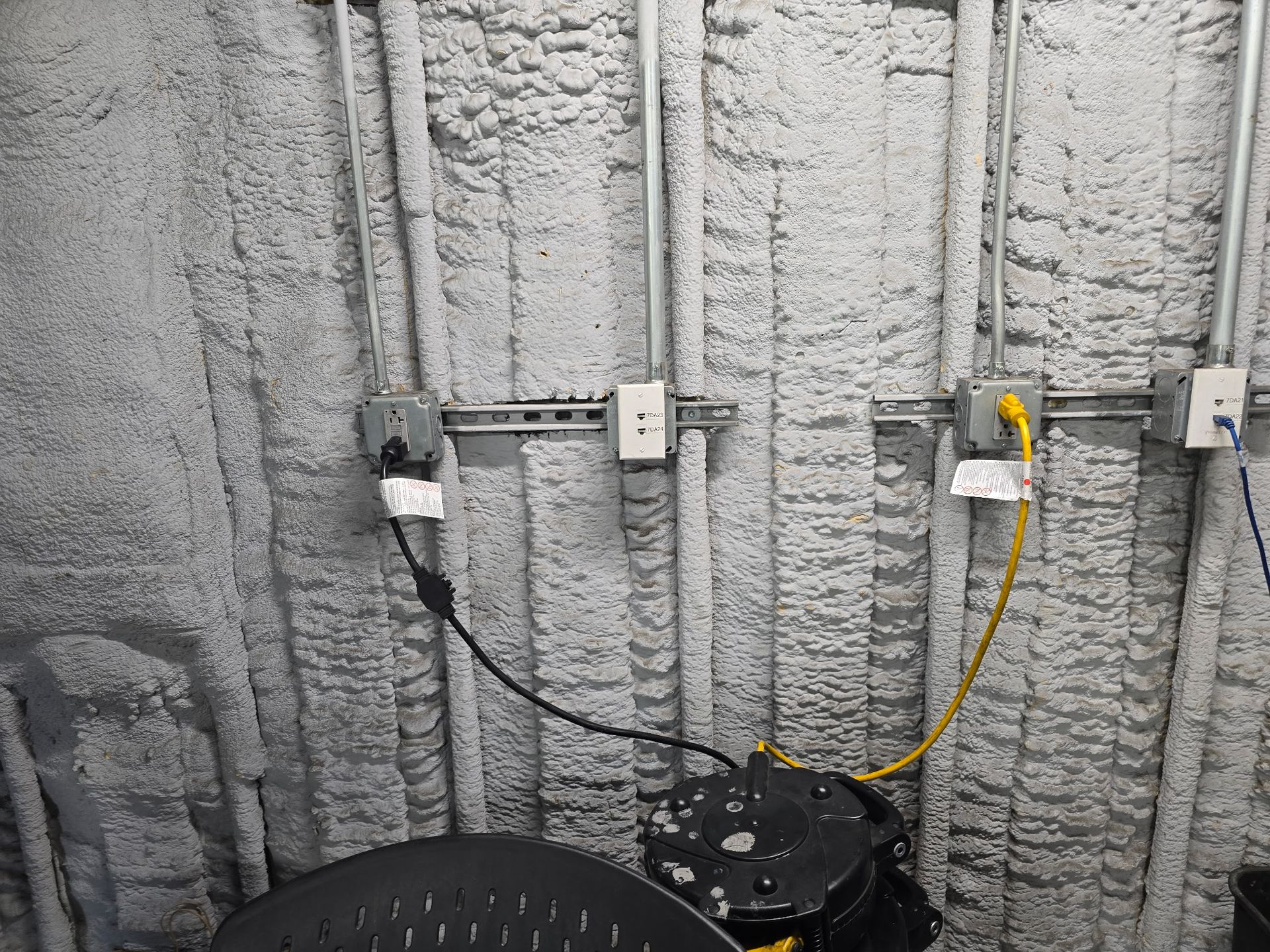 Utility wall with exposed wiring, outlets, and two cords connected to black equipment on the floor.