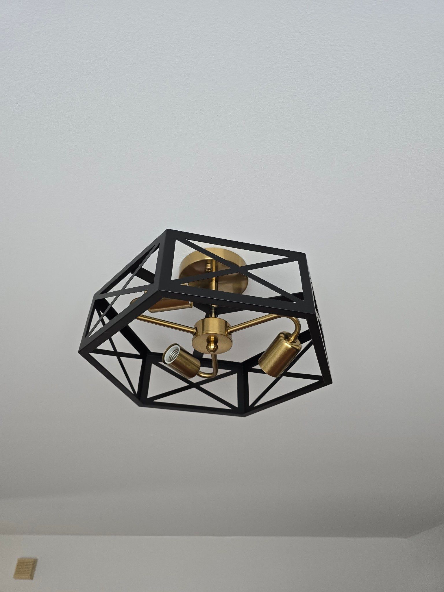 Black geometric ceiling light fixture with brass accents on a white ceiling
